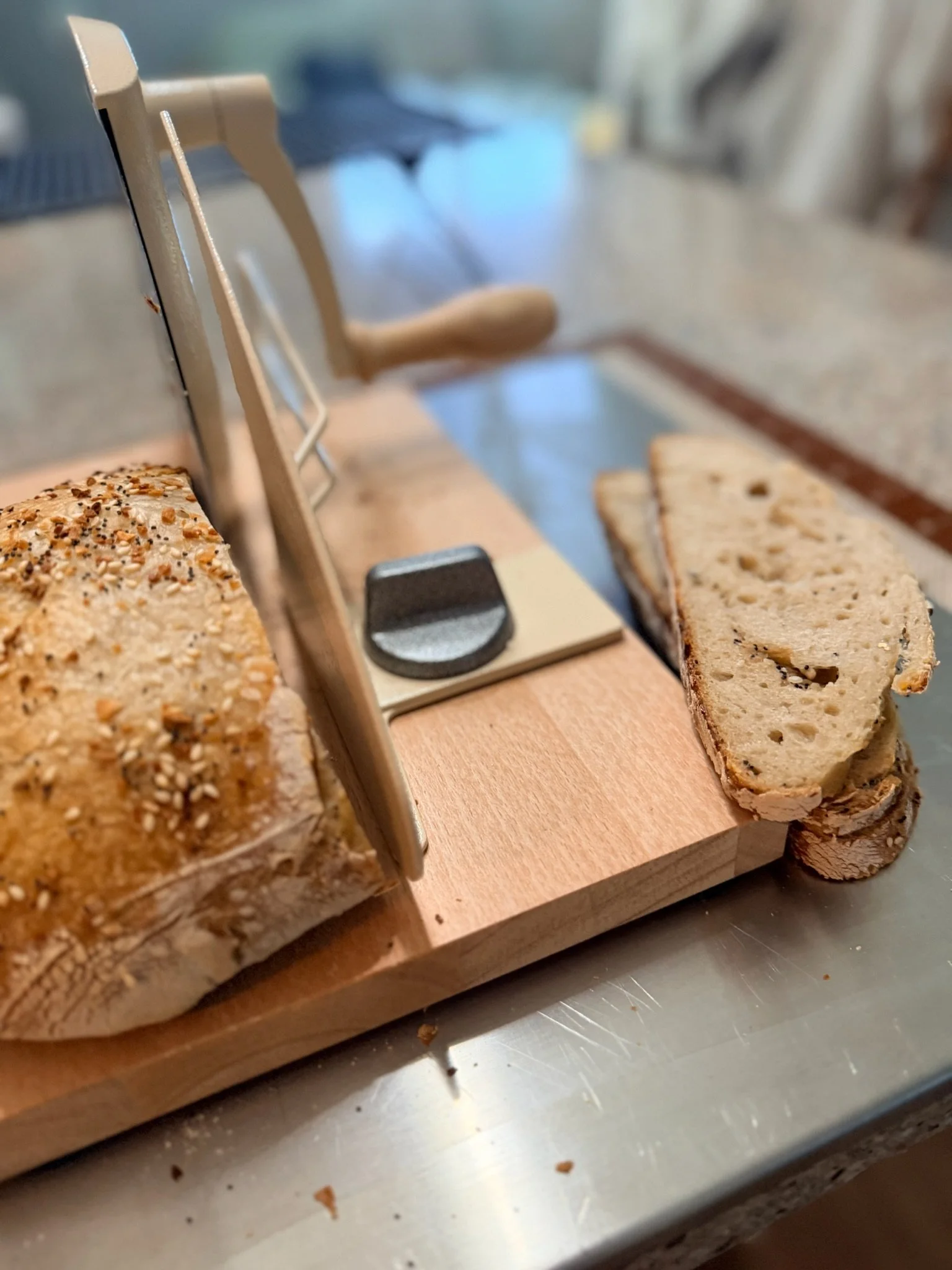 Close-up of sliced multi-grain bread on a wooden cutting board, with a bread slicer in the background.