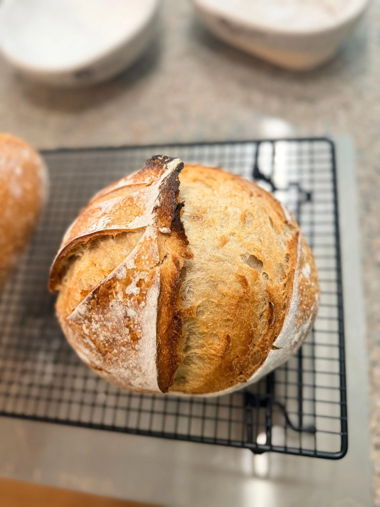 A rustic loaf of bread with a crusty exterior and a slightly burnt top, resting on a wire cooling rack.
