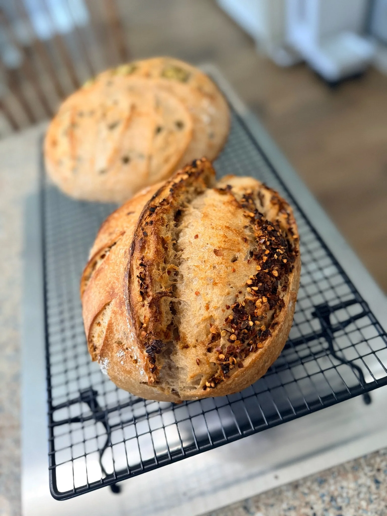 Fresh baked bread with a crust topped with chili flakes resting on a cooling rack.