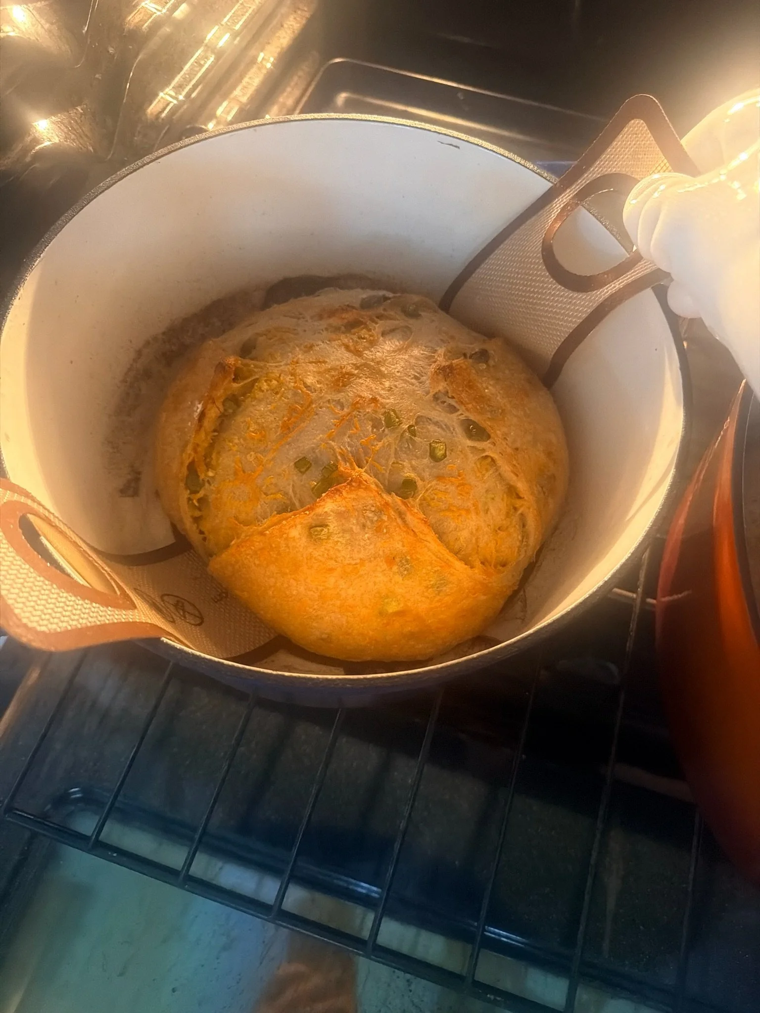A pot in the oven containing a partially cooked bread, with a golden-brown crust on top.