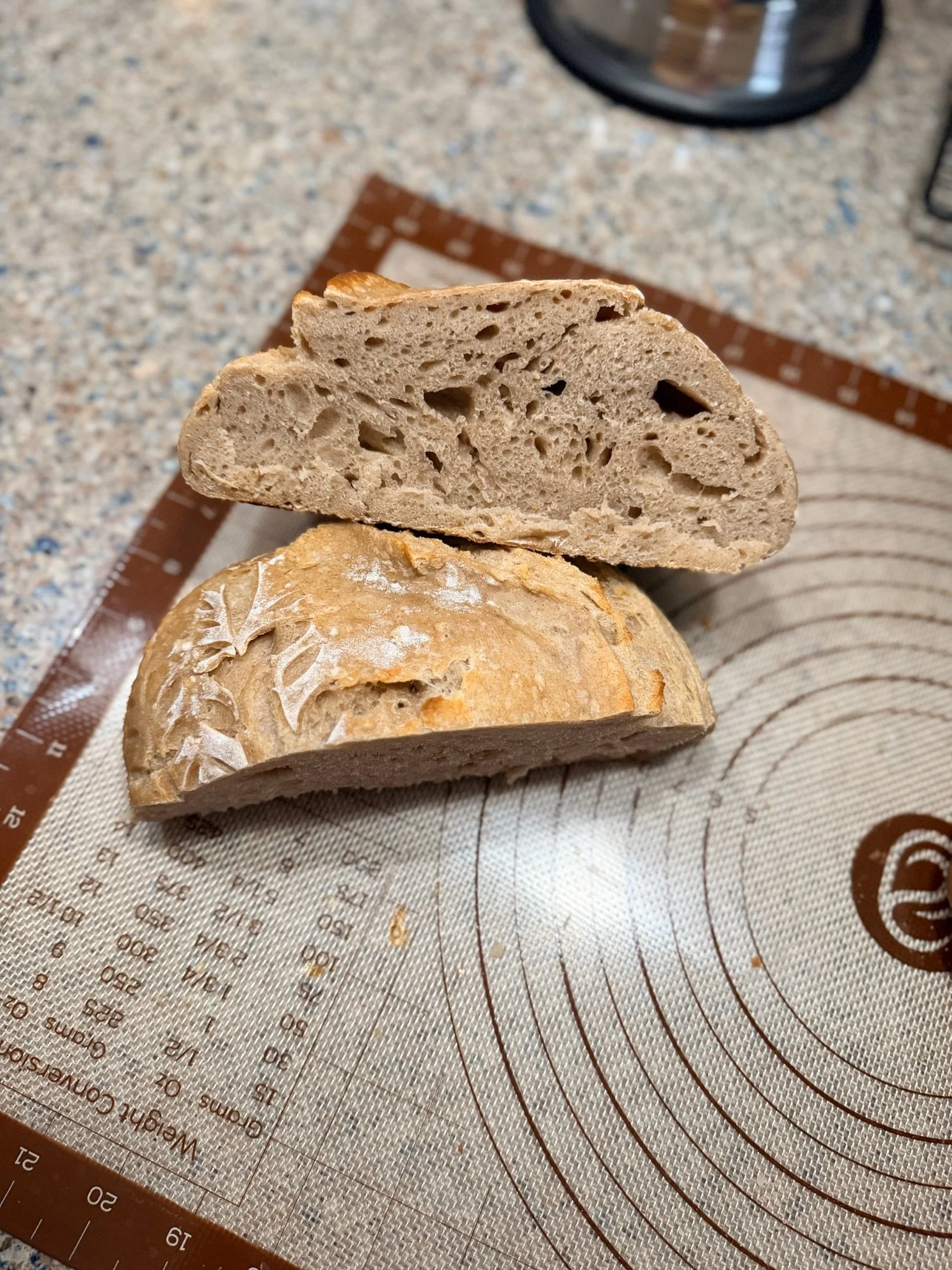 A piece of baked bread with a crusty exterior and a soft interior, placed on a patterned baking mat on a kitchen countertop.