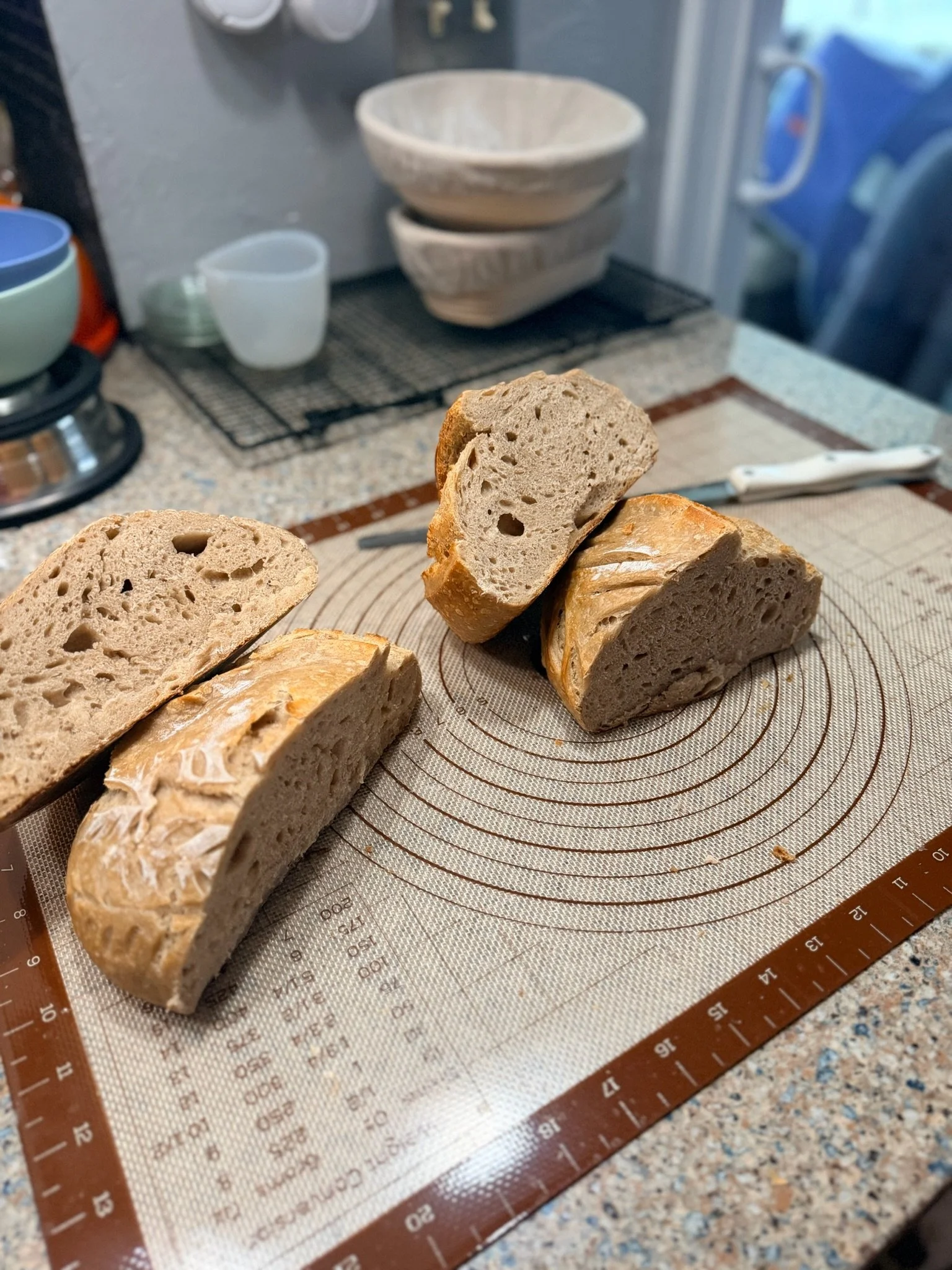 Sliced loaf of bread on a silicone baking mat on a kitchen counter with bread crumbs around.