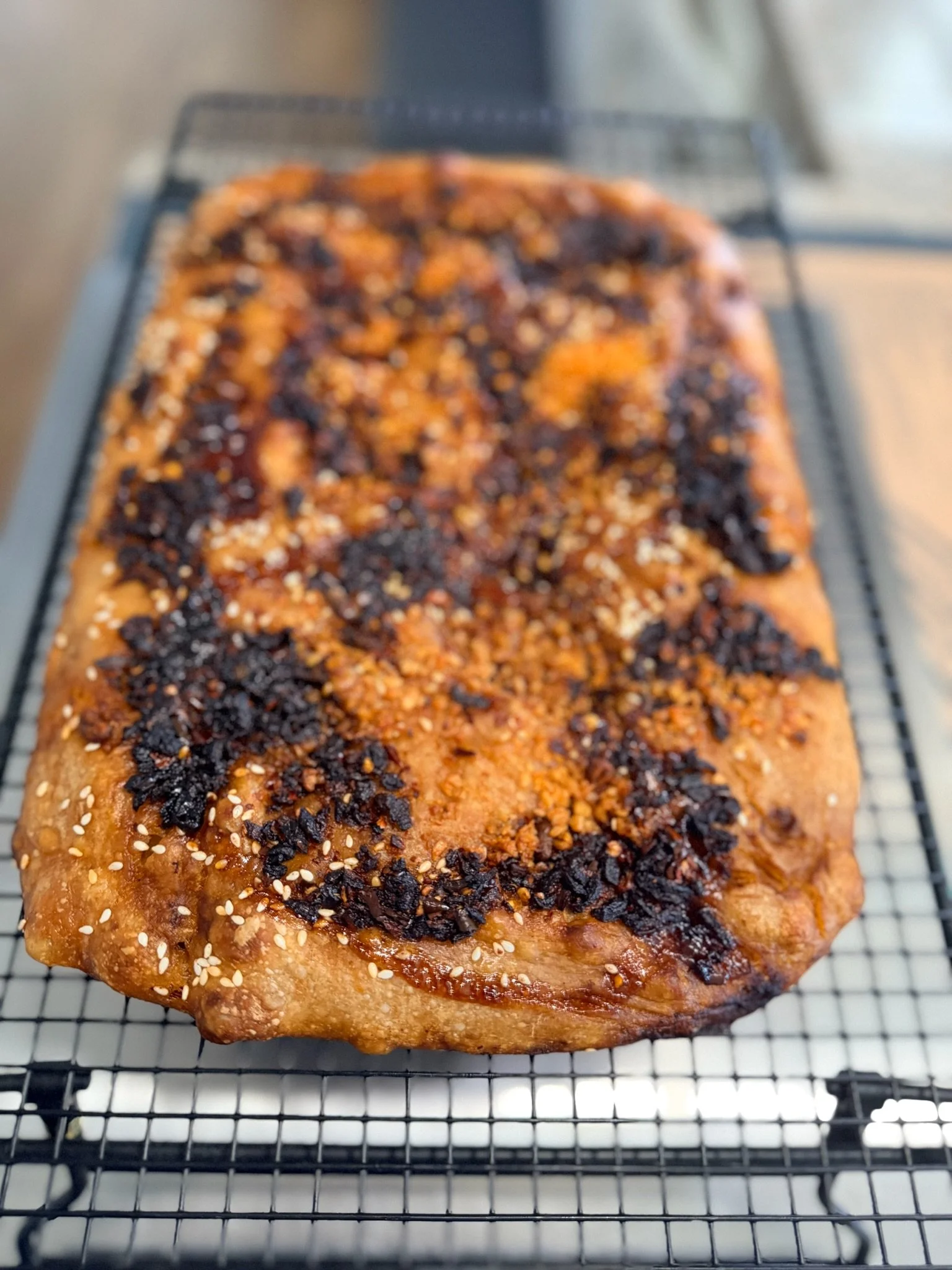 Baked bread topped with caramelized sugar, chopped nuts, and caramelized fruit, resting on a cooling rack.