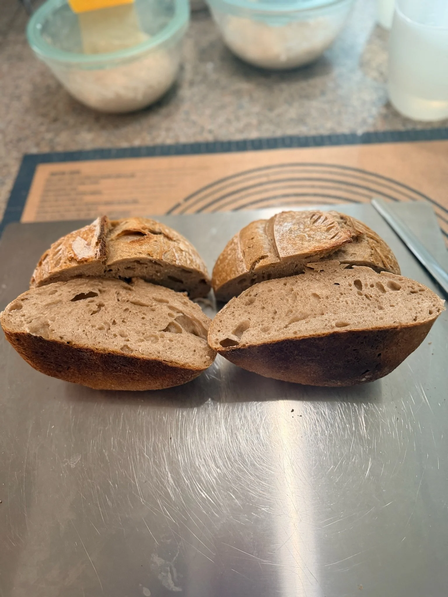 Two halves of a sliced loaf of bread on a metal surface, with background containing bowls and kitchen items.