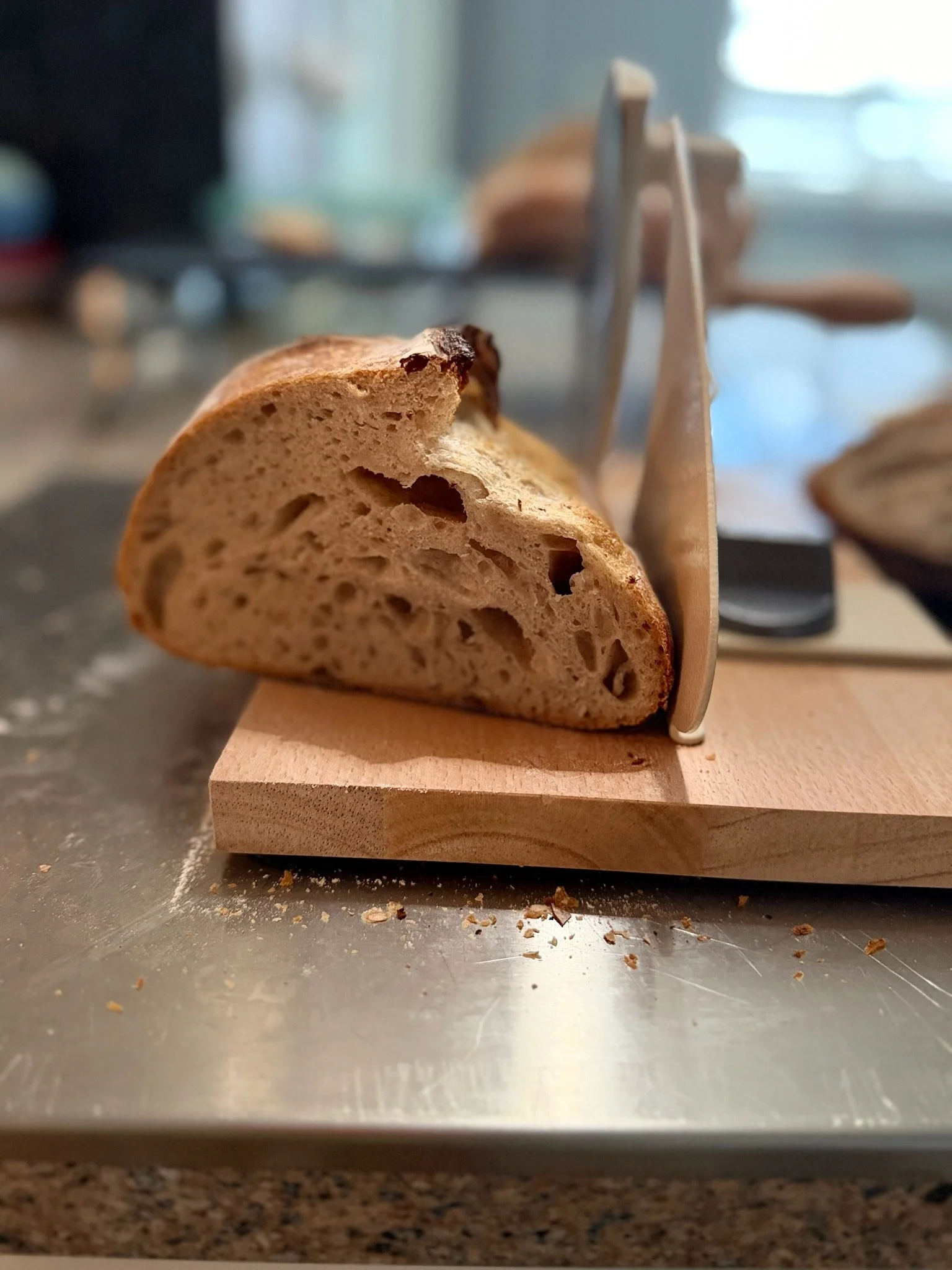 Close-up of a slice of bread on a wooden cutting board with a bread knife in the background.