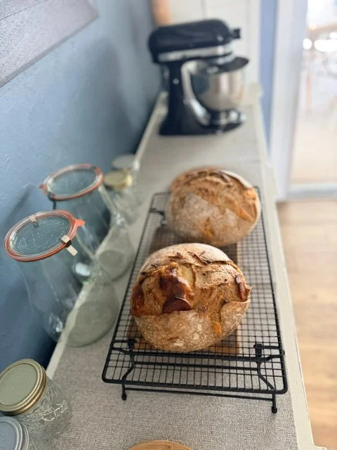 Two freshly baked bread rolls on a wire cooling rack on a kitchen counter near a stand mixer and glass jars.