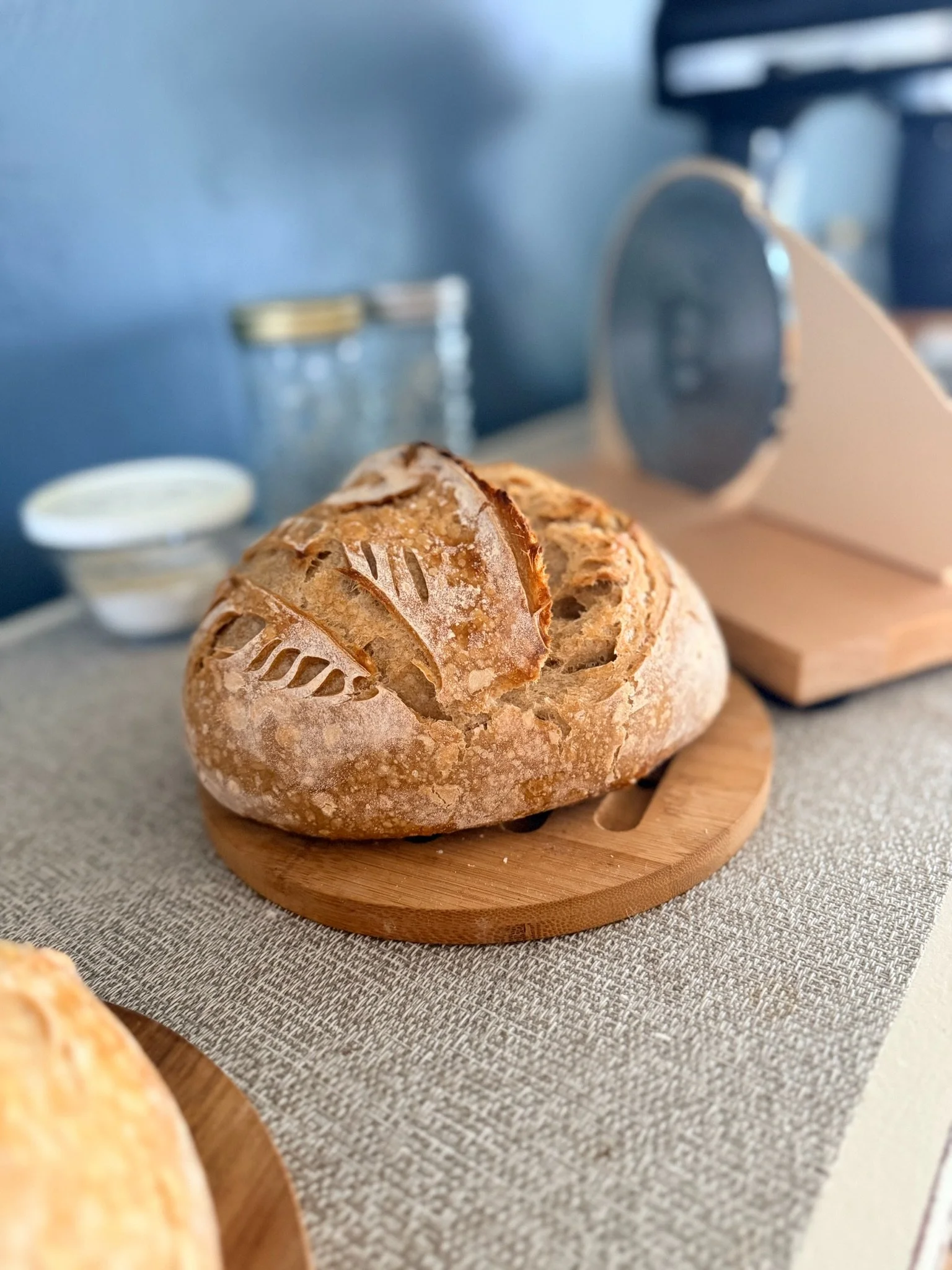 A close-up of a round loaf of bread with a crusty top sitting on a wooden board, with a toaster in the background.