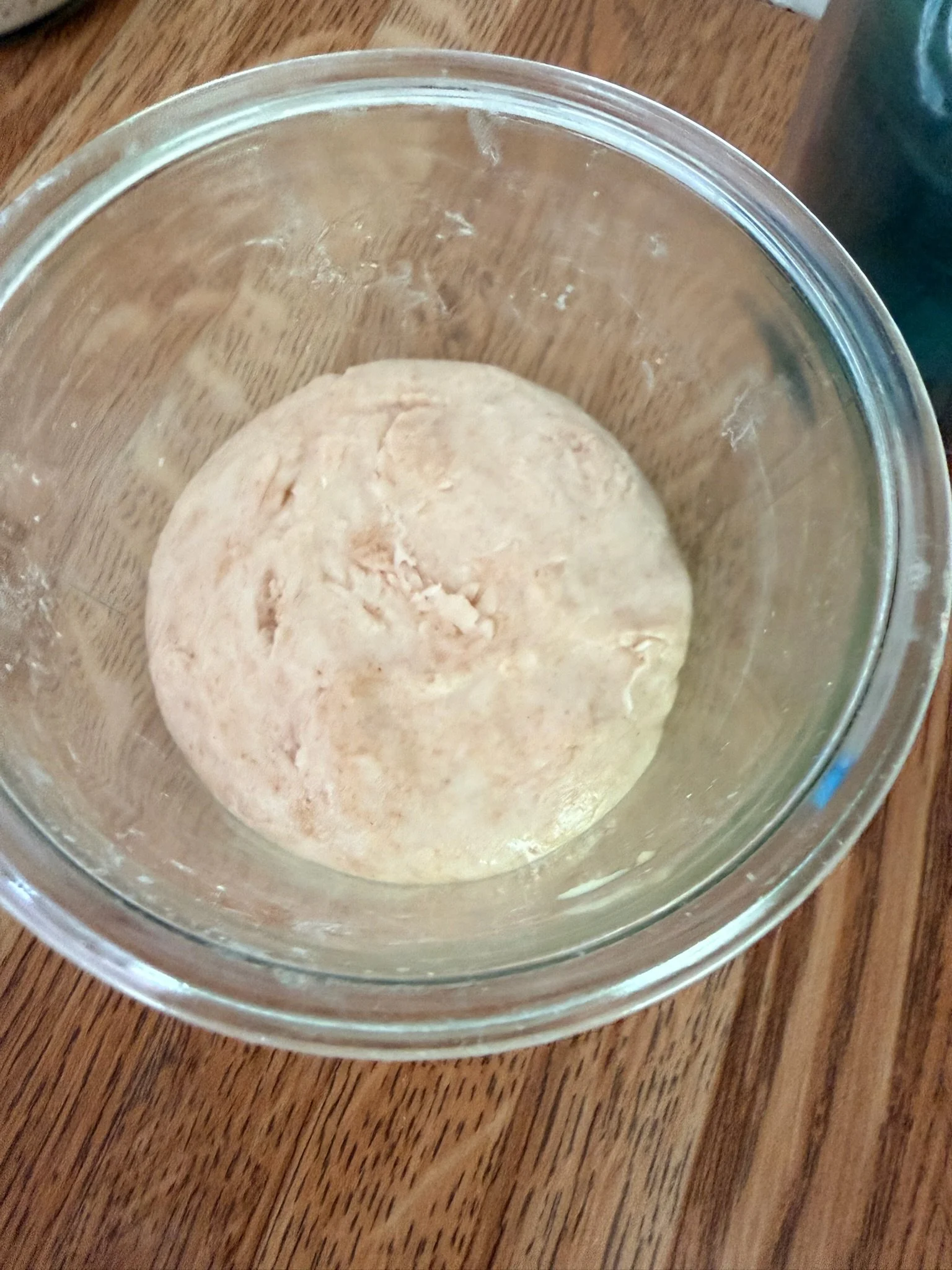 A ball of dough inside a glass bowl on a wooden surface.