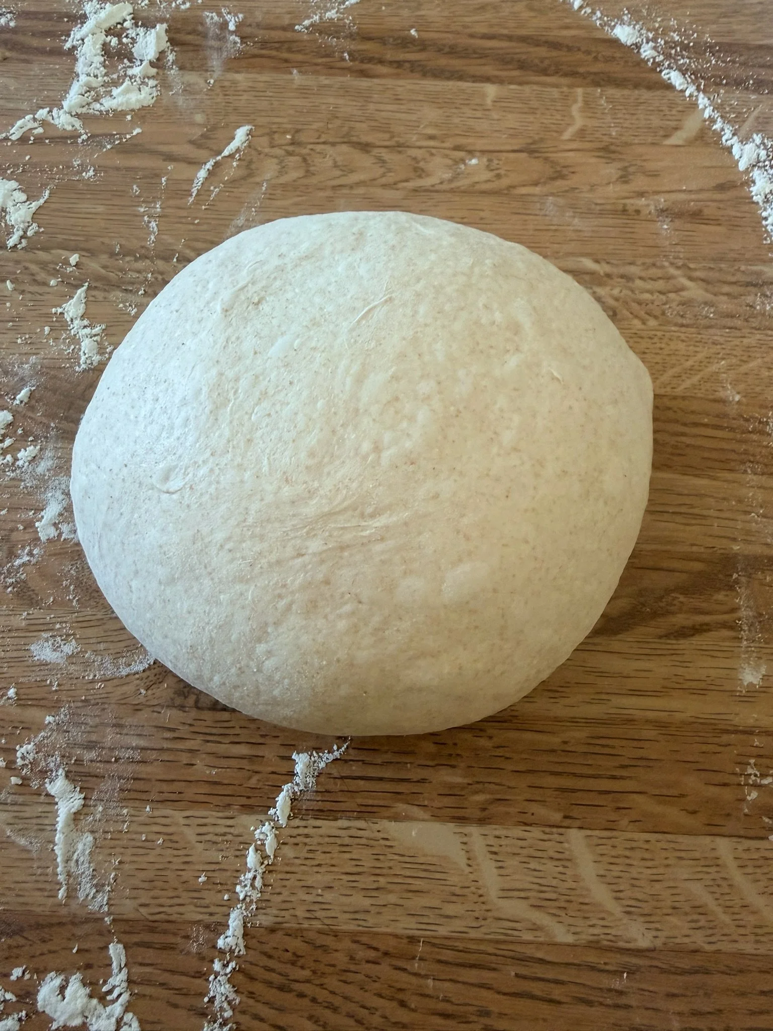 A round ball of dough on a wooden surface with flour scattered around.
