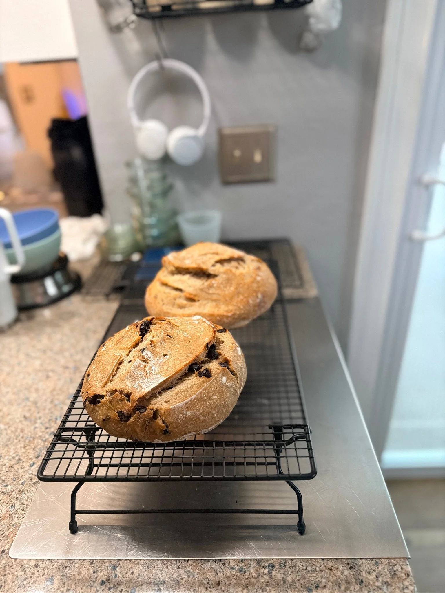 Two loaves of bread on a cooling rack in a kitchen.