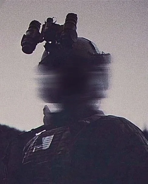 Silhouette of a soldier wearing helmet and tactical gear, holding binoculars, with a blurred background.