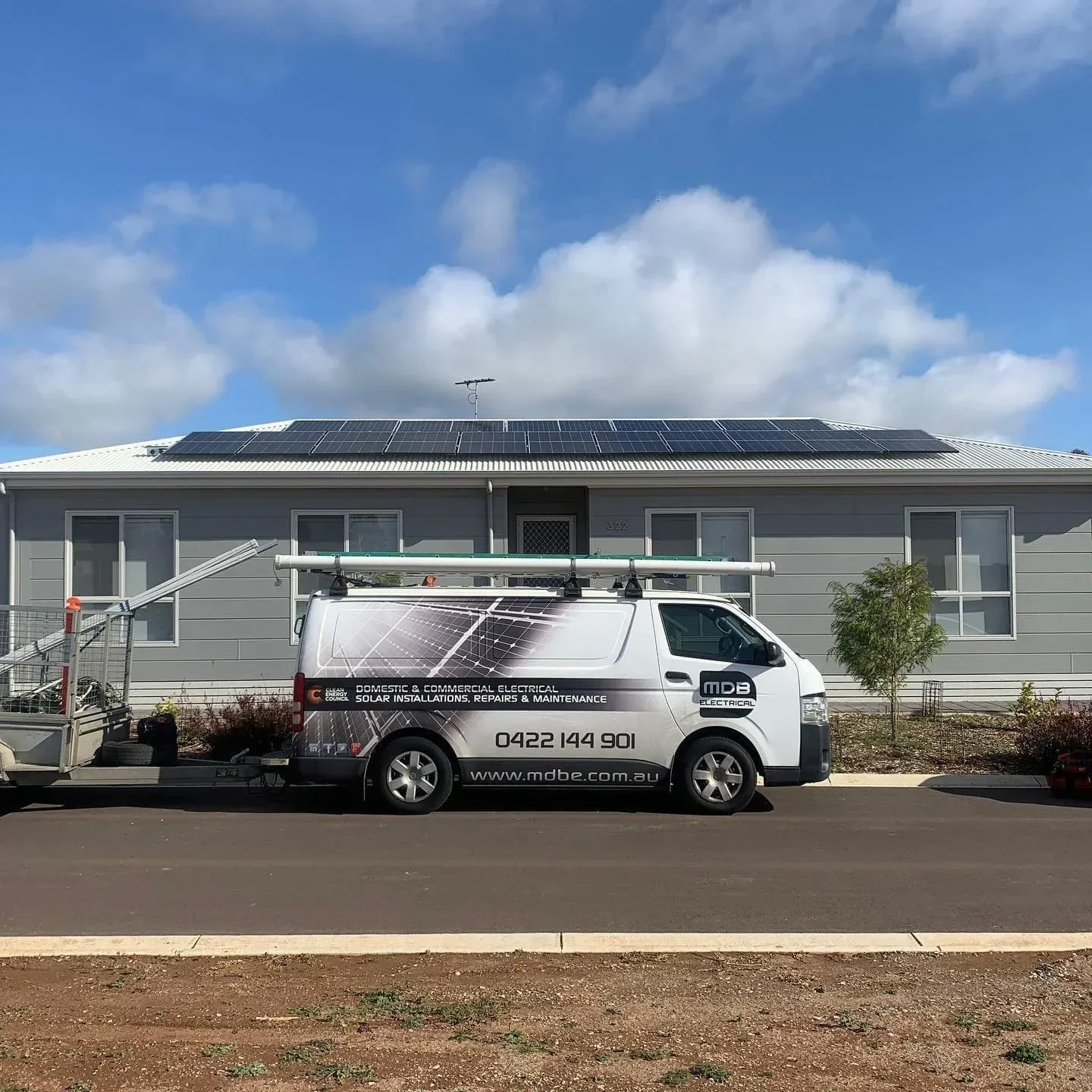 White van with company branding parked in front of a house with solar panels on the roof, blue sky with clouds overhead.
