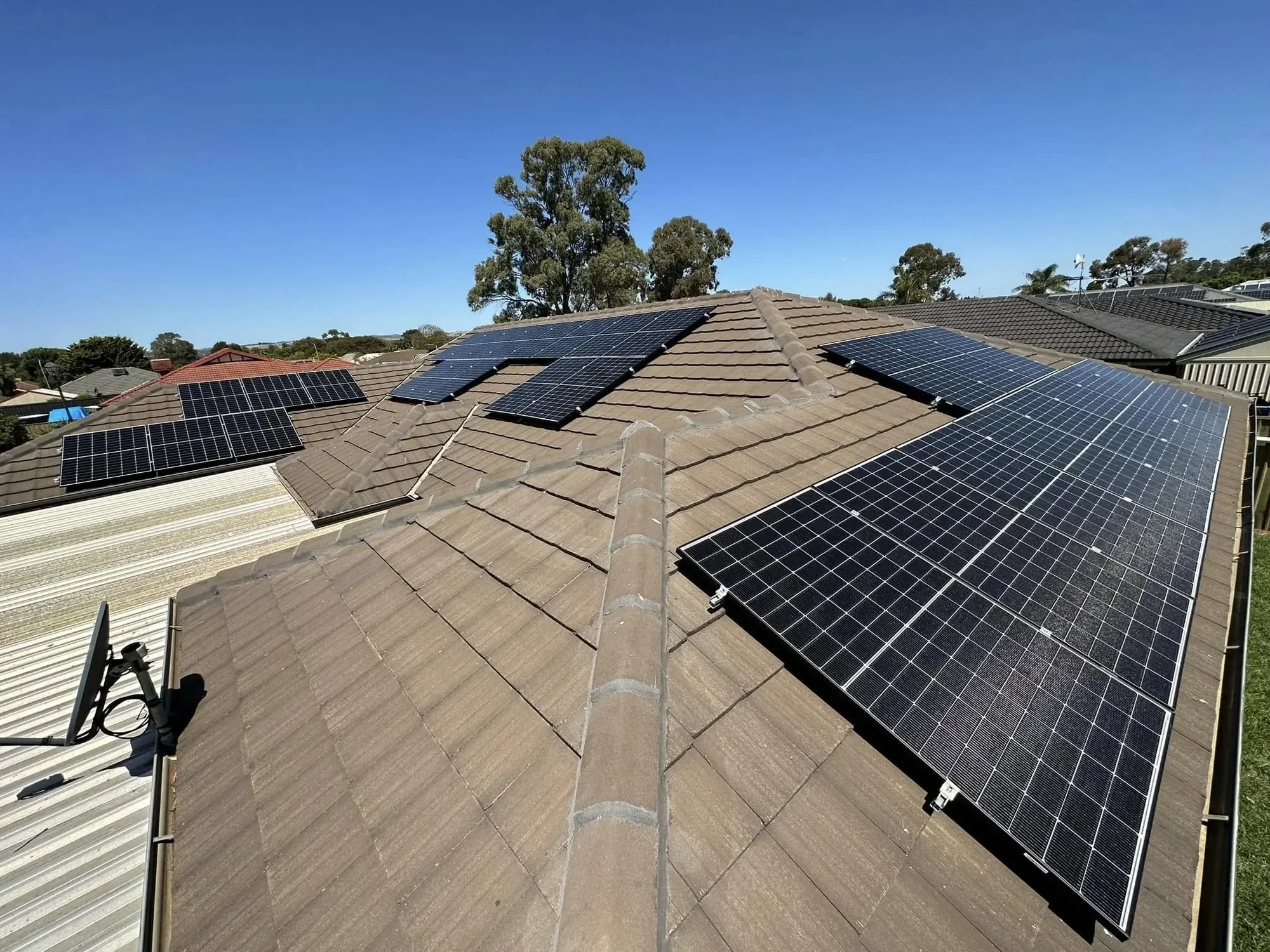 Several solar panels installed on a residential house roof under a clear blue sky.