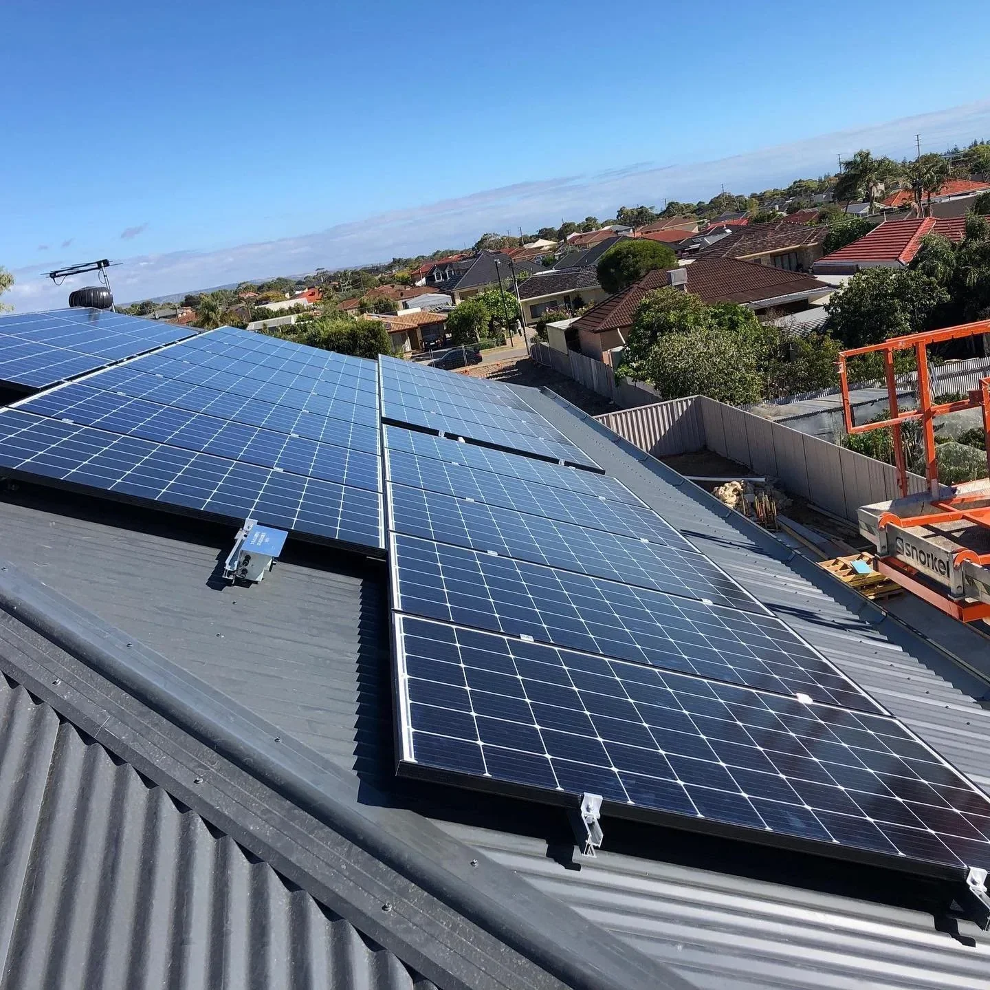 Solar panels installed on a gray rooftop in a residential neighborhood under a clear blue sky.