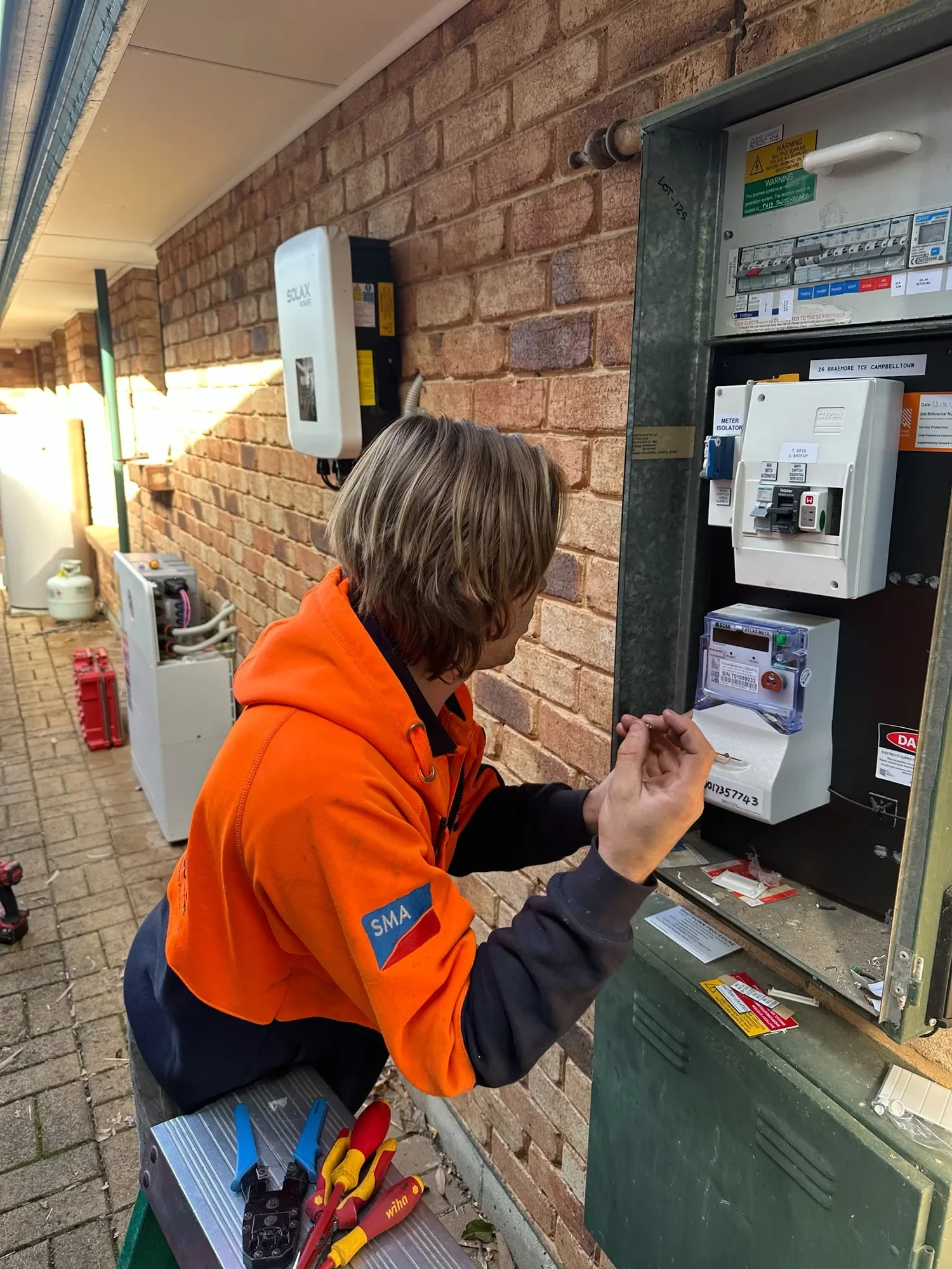 Person working on an electrical panel outside a brick building with a brick wall in the background.