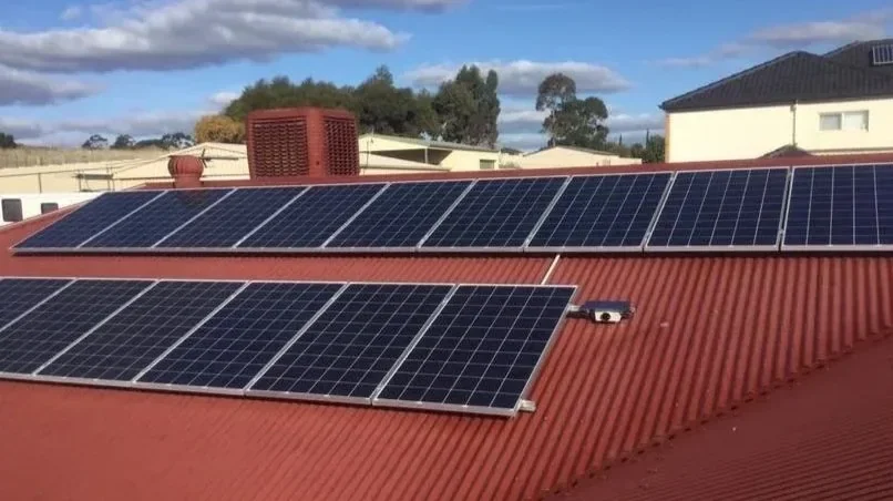 Multiple solar panels installed on a red metal roof.