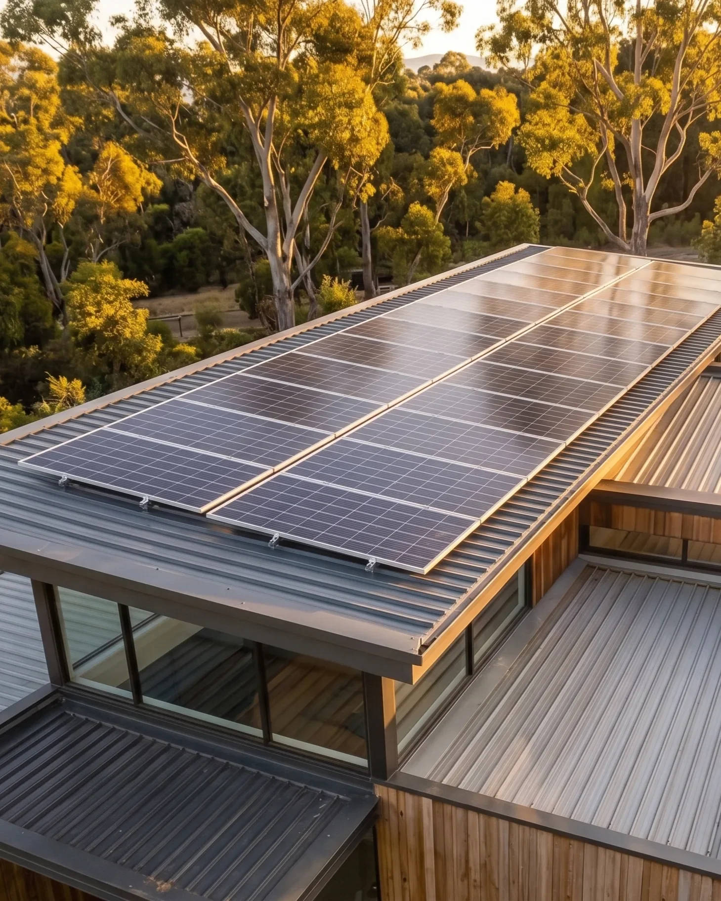 Solar panels installed on the roof of a modern house with glass walls, overlooking a forest with trees and hills in the background during a sunny day.