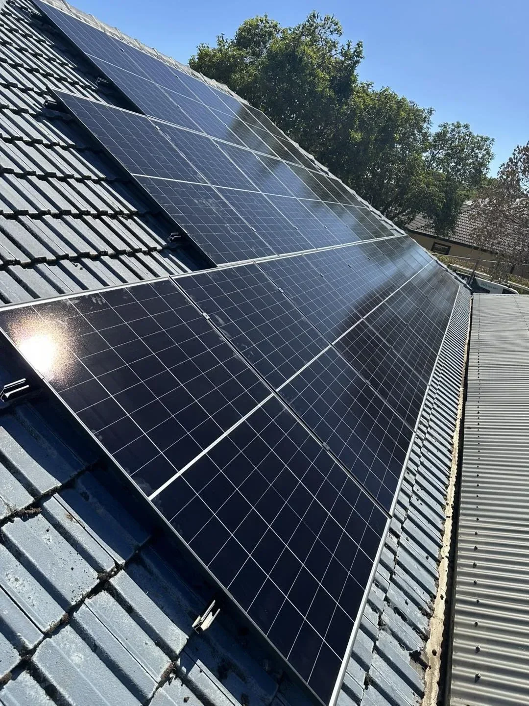 Several solar panels installed on a sloped rooftop, with trees and a clear blue sky in the background.