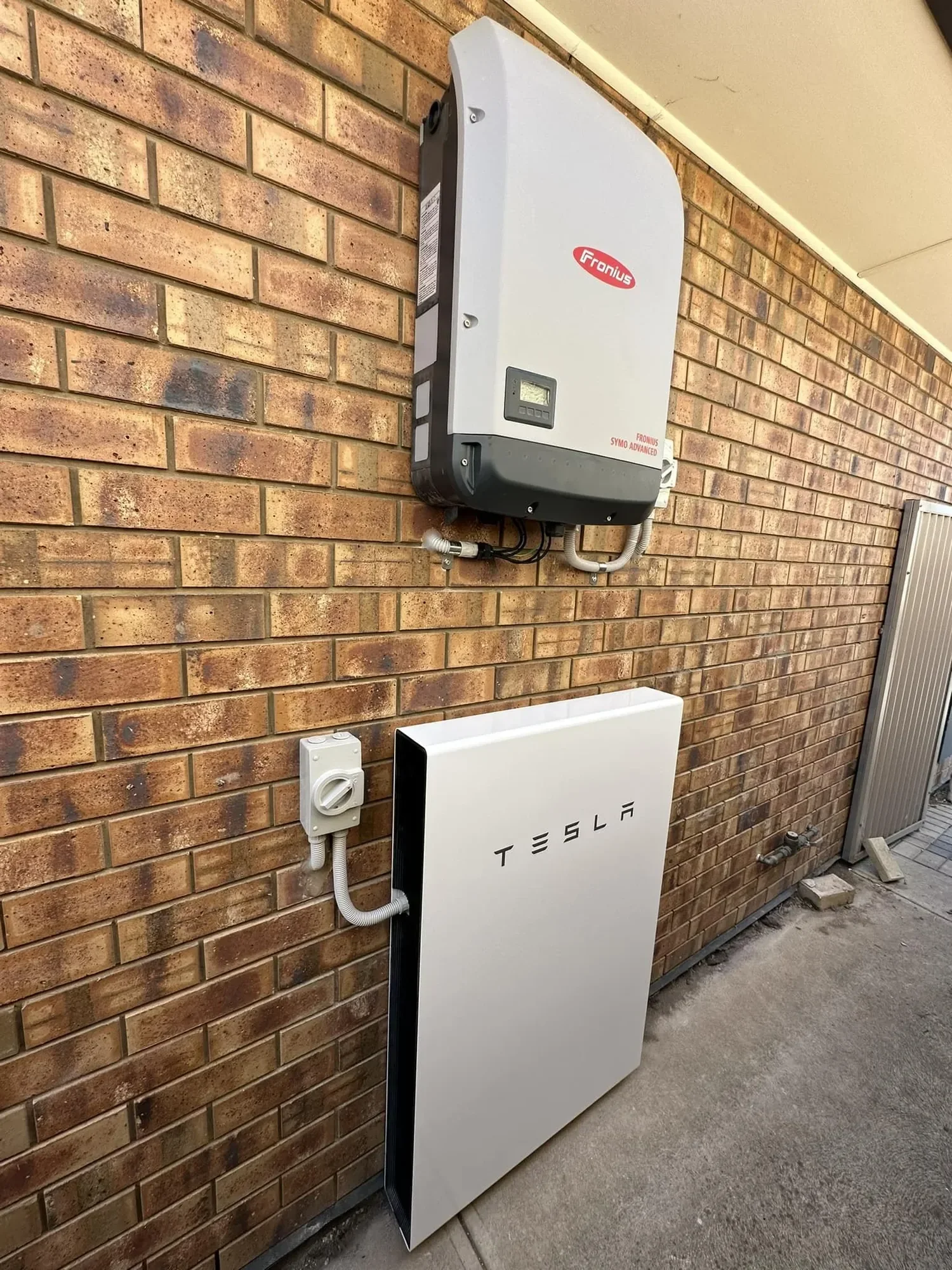 A Tesla Powerwall and a Fronius Symo Advanced solar inverter installed on a brick wall.
