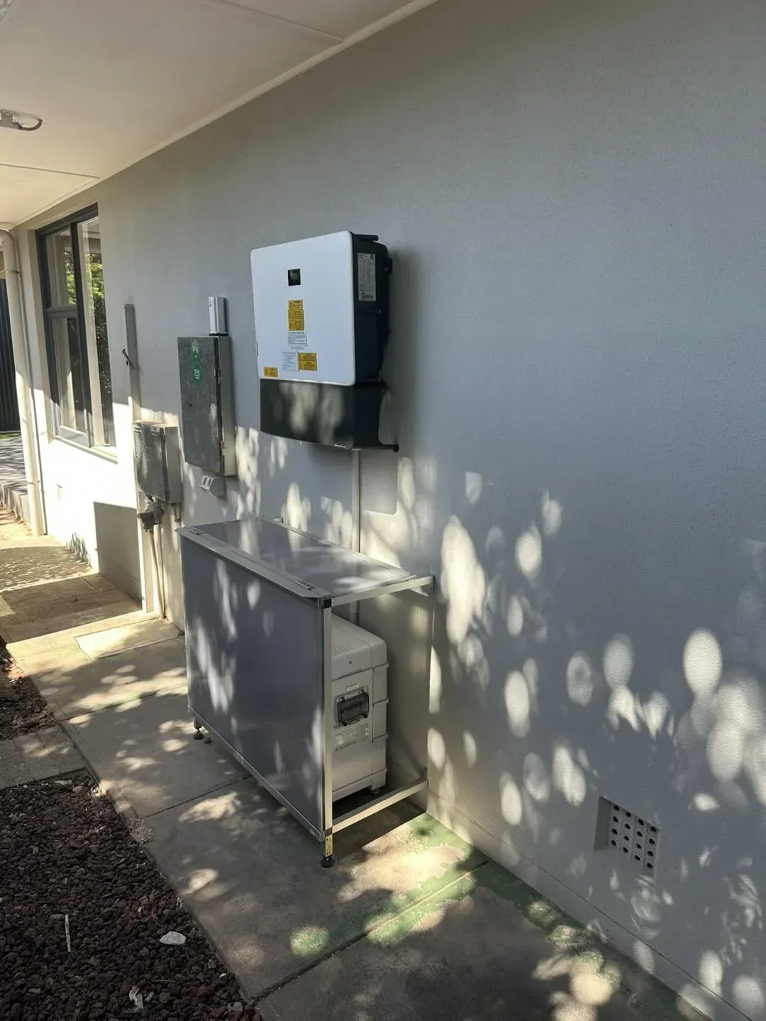 Outdoor electrical and utility box on exterior wall of building, with shaded shadows on wall and ground.