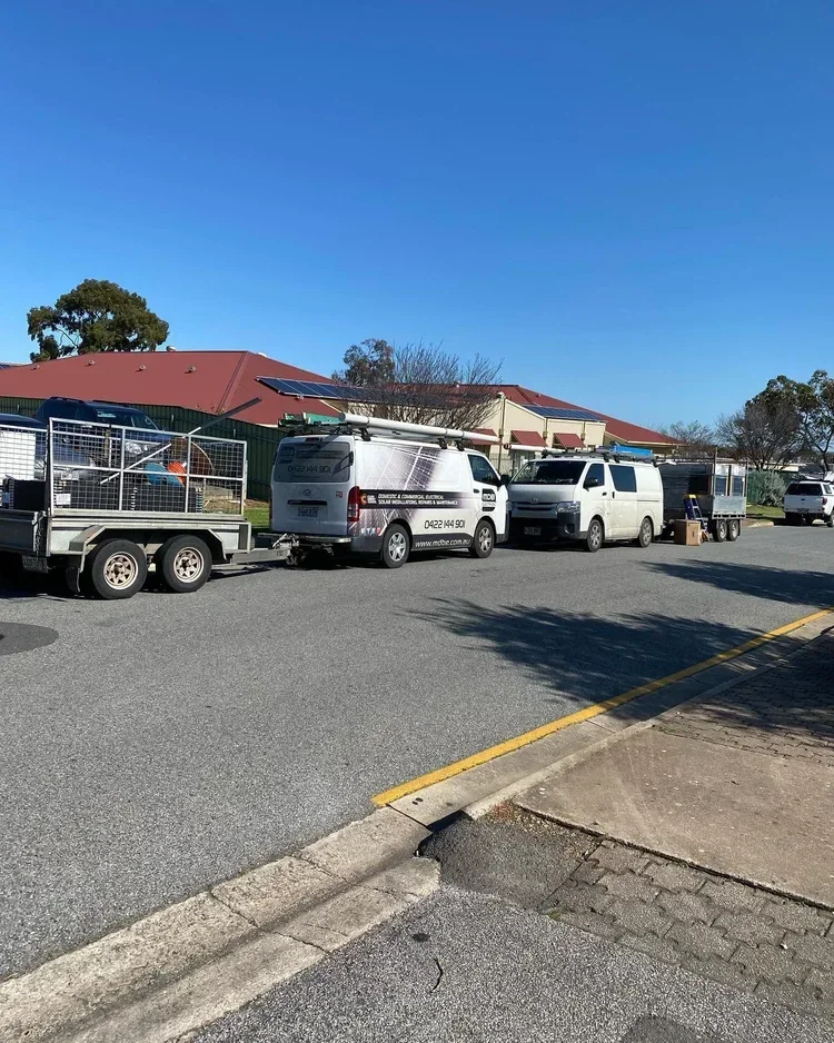 A parking lot with several parked service vehicles, including vans with equipment, and a small trailer, under a clear blue sky.