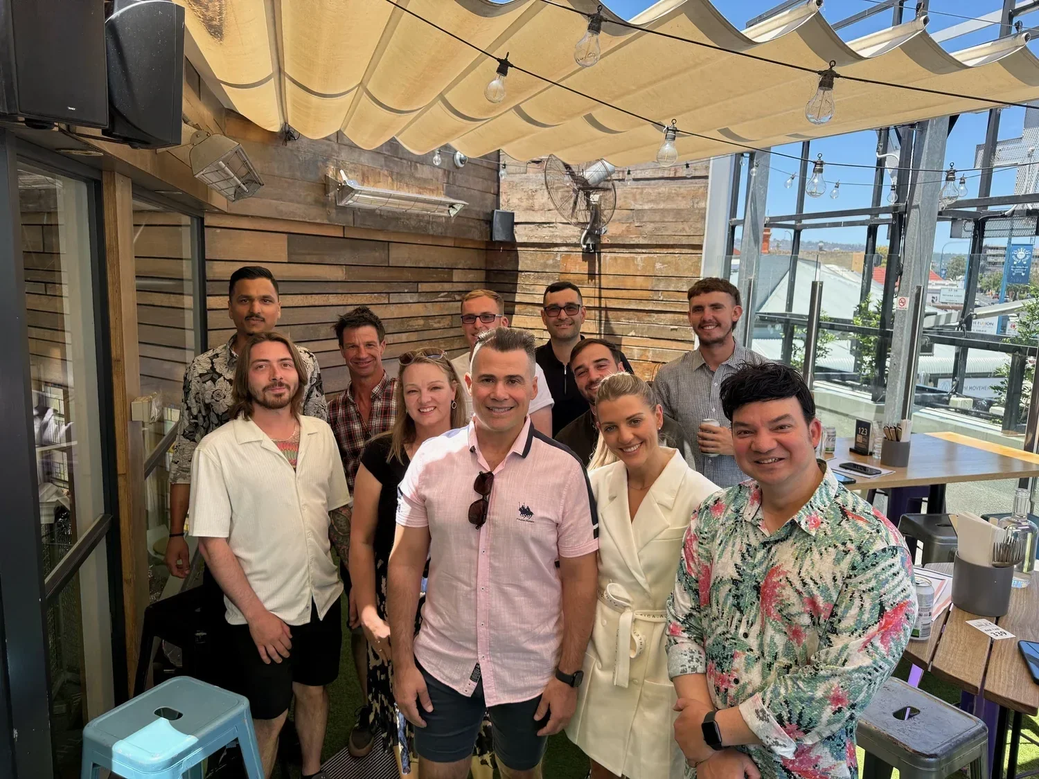 Group of people smiling inside a restaurant or cafe with large windows and outdoor view.