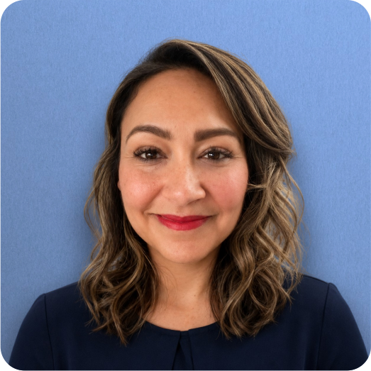 A woman with wavy brown hair and red lipstick smiling at the camera with a solid blue background.