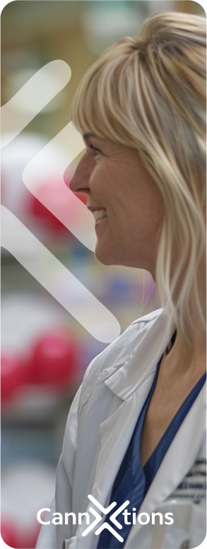 A woman with blonde hair smiling and wearing a white medical coat in a clinical setting.