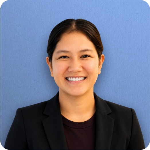 A young woman with dark hair smiling, wearing a black blazer against a blue background.