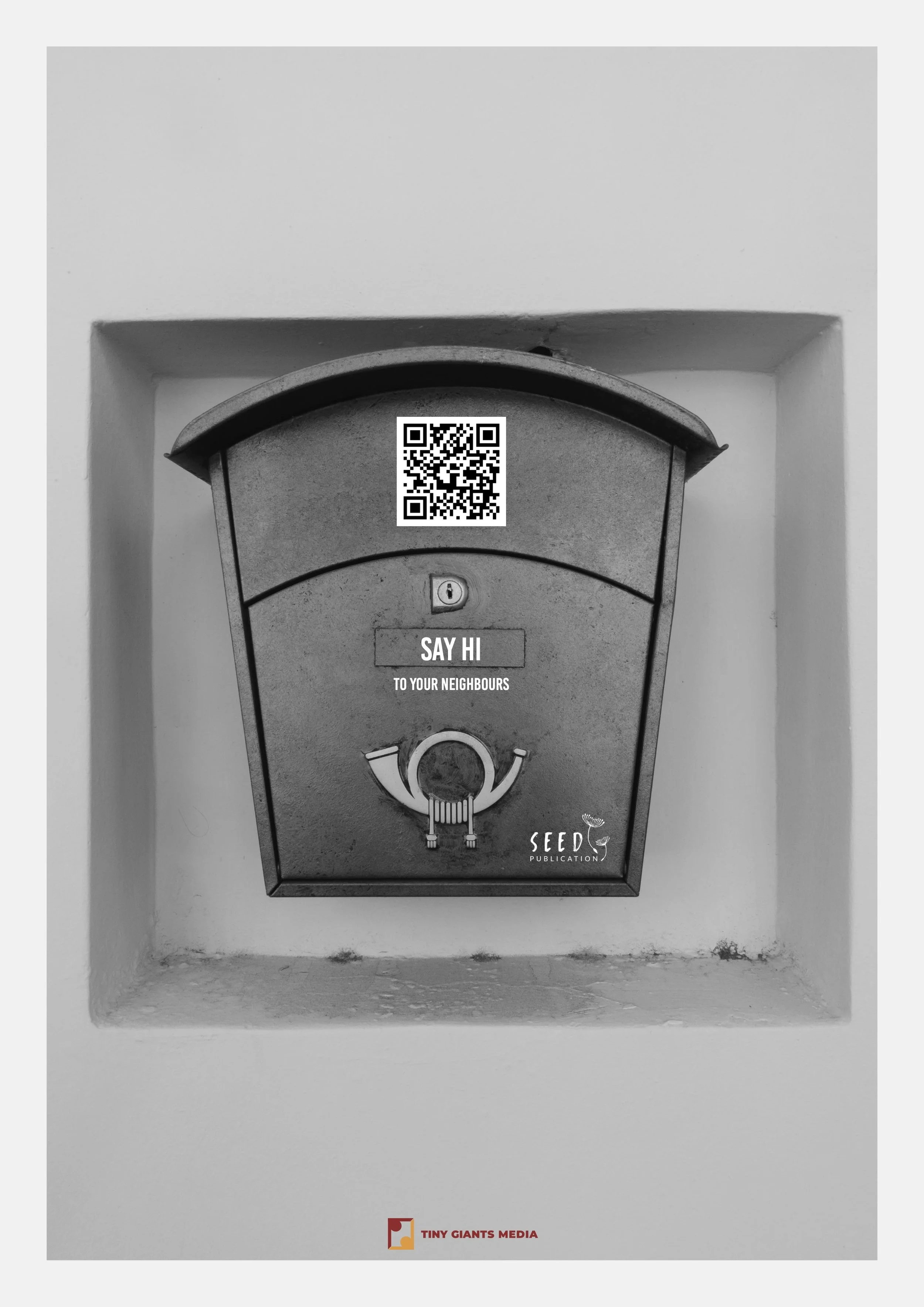 Black and white photo of a mailbox with a QR code sticker on it, located in a recessed wall slot. The mailbox has a small lid, a lock, and a handle. Below it is a label that reads 'SAY HI TO YOUR NEIGHBOURS' with the logo 'SEED PUBLICATION' at the bo