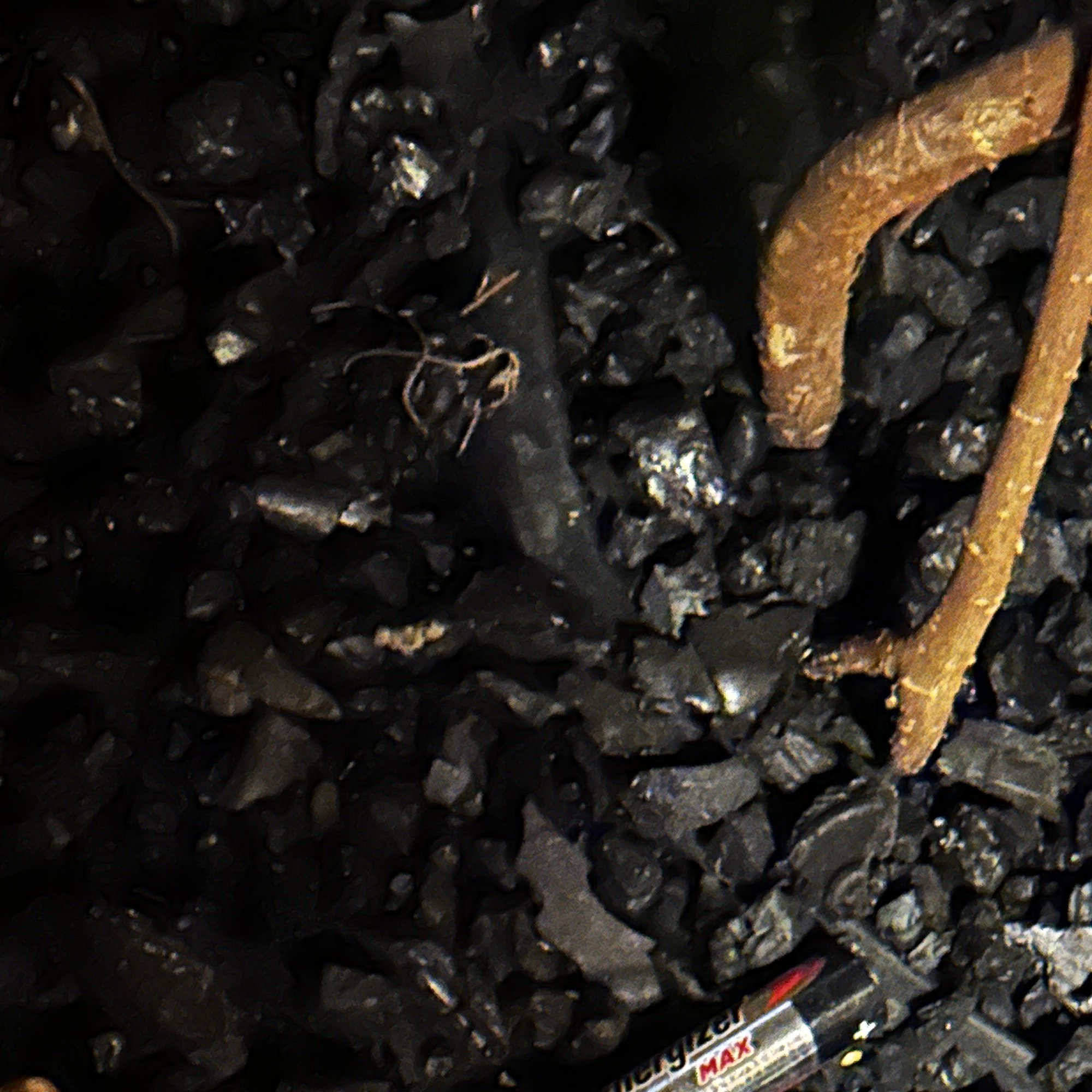 Close-up of black gravel and a rusty metal object, possibly a tool or piece of machinery, with part of a measuring cup labeled 'MAX' visible at the bottom.