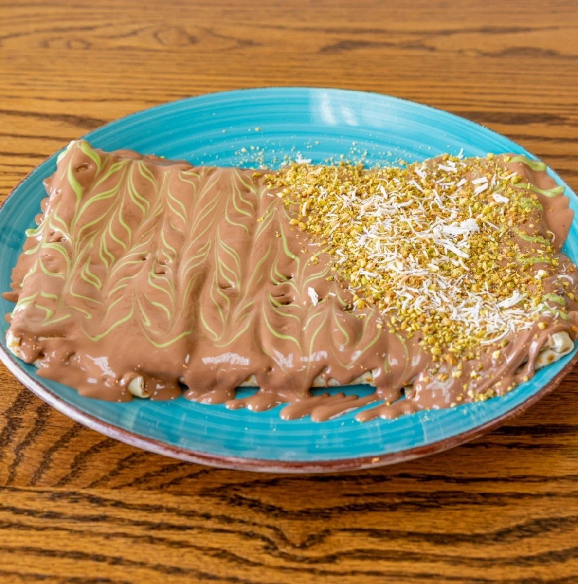 A large chocolate and vanilla ice cream dessert topped with crushed pistachios and shredded coconut on a blue plate.