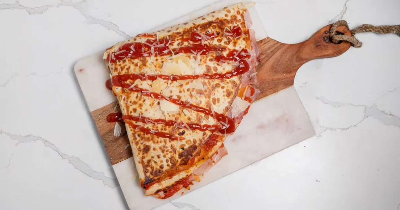 A slice of pizza with cheese, tomato sauce, and drizzled ketchup on a wooden paddle serving board.