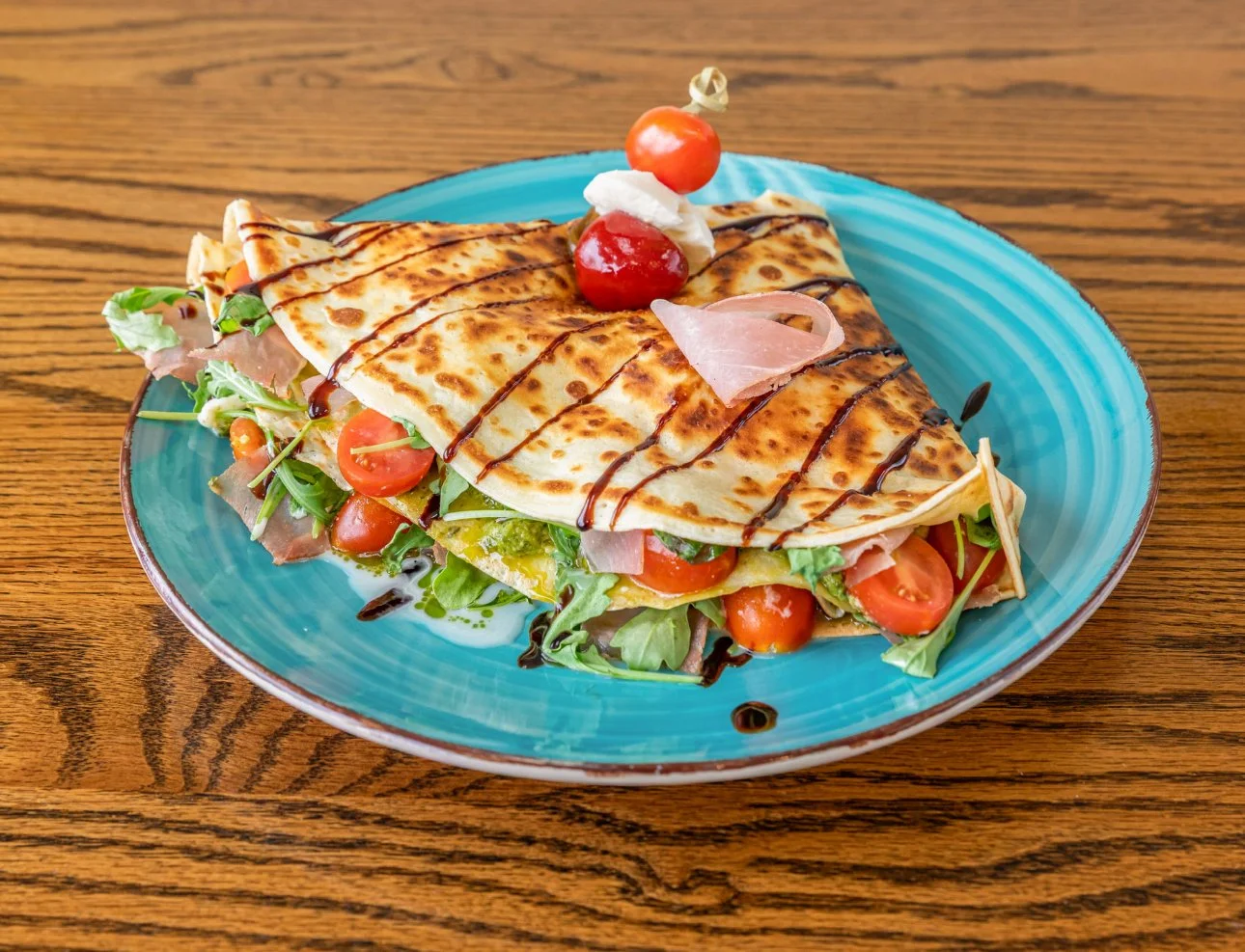 Quesadilla with cherry tomatoes, lettuce, and drizzled with balsamic vinegar on a turquoise plate.