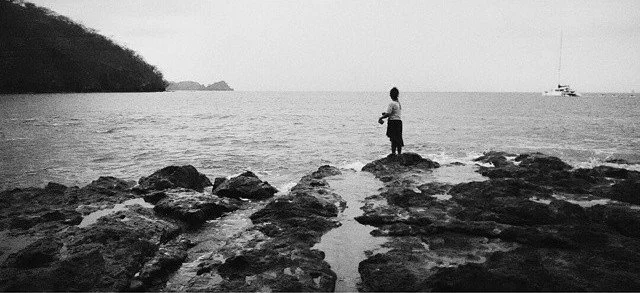 Solitary figure standing on rocks overlooking the ocean