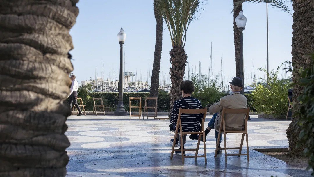 Two people sitting quietly on a bench along a coastal promenade