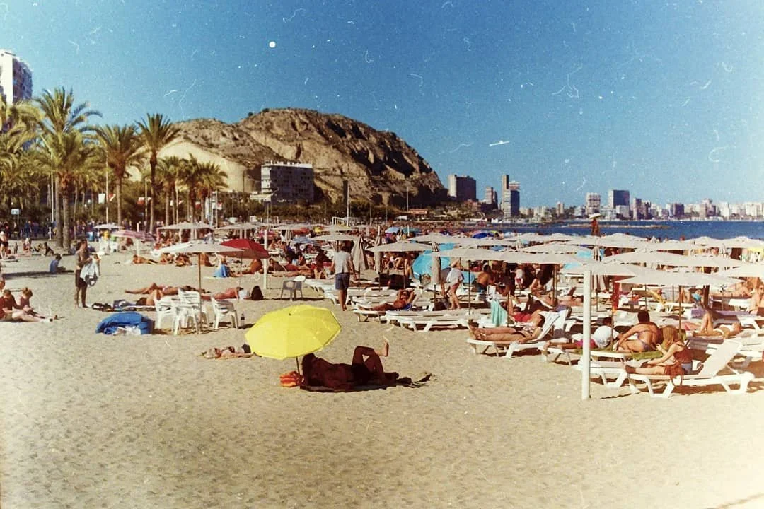 Beachgoers enjoying the Mediterranean coastline in Alicante, Spain, featured in Between Two Shores.