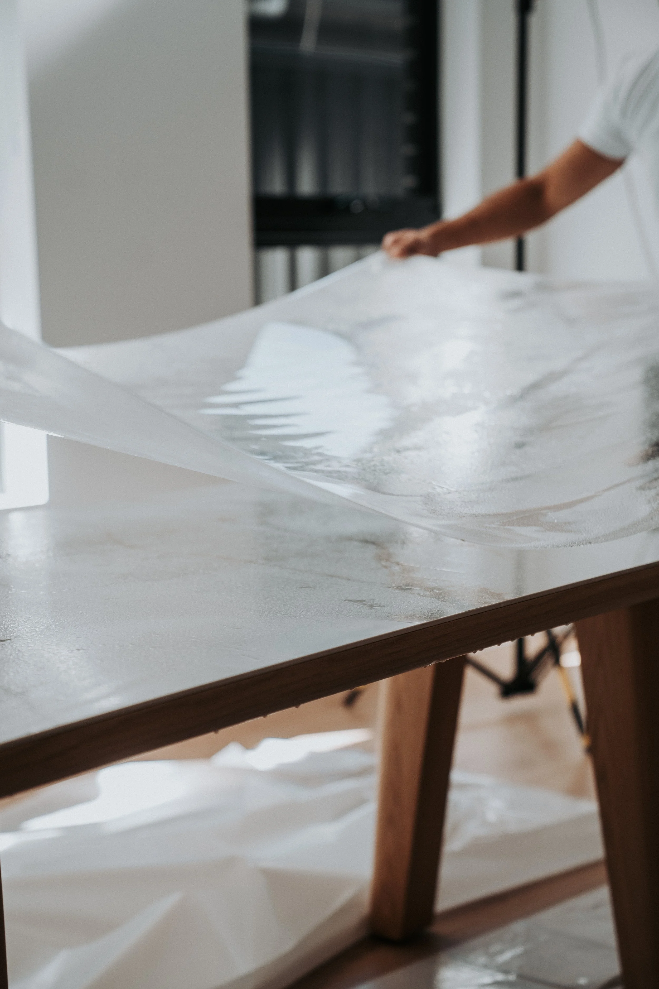 Person wiping down a white surfboard with a cloth on a wooden table.