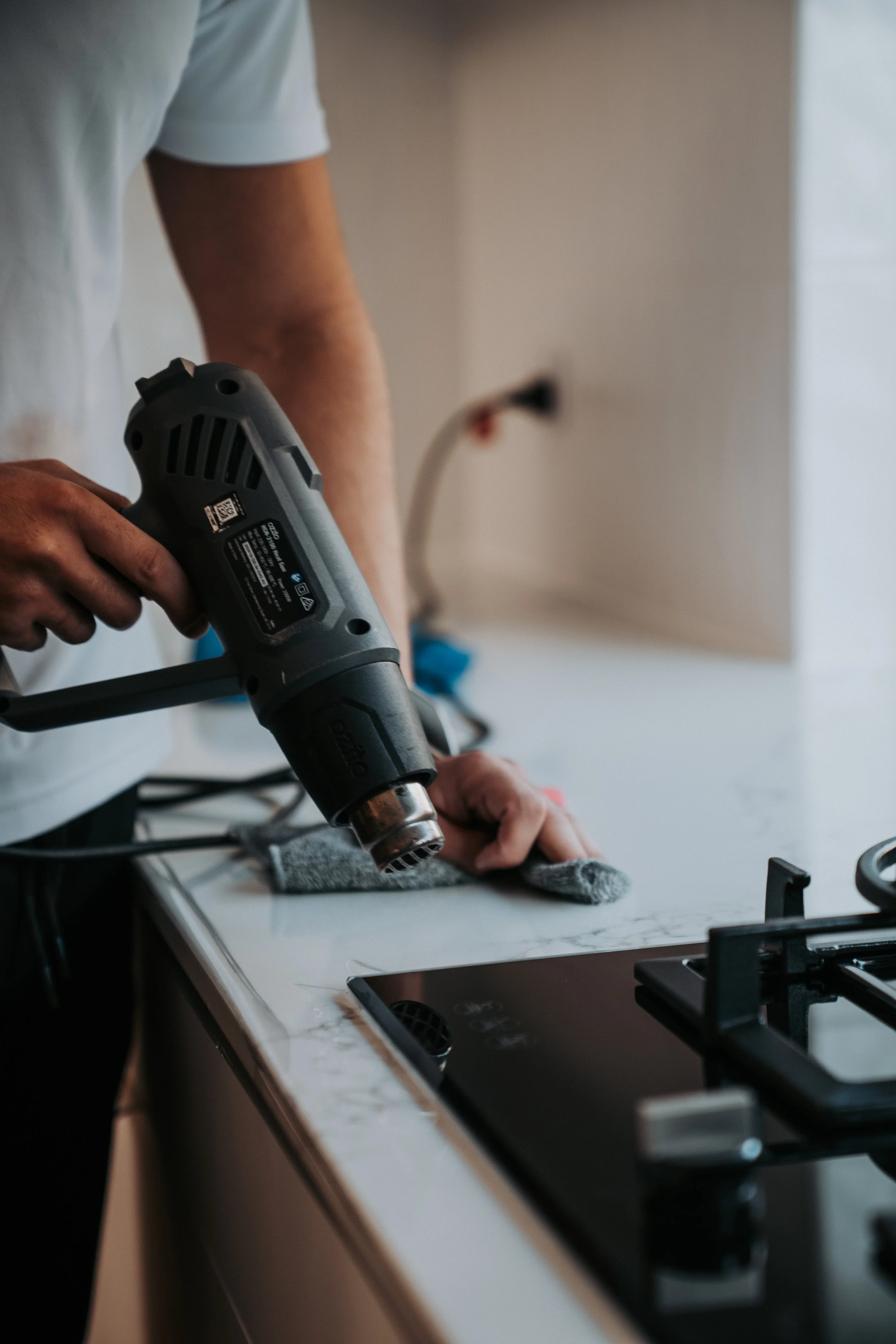 A person holding a heat gun over a garment on a table in a kitchen or workshop.