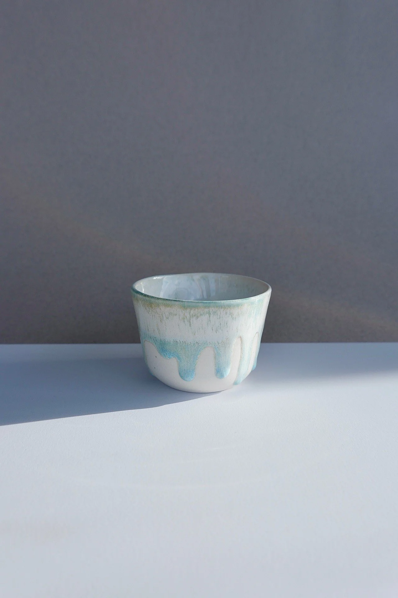 A white ceramic bowl with blue and green glaze drips, placed on a white surface with a grey background.