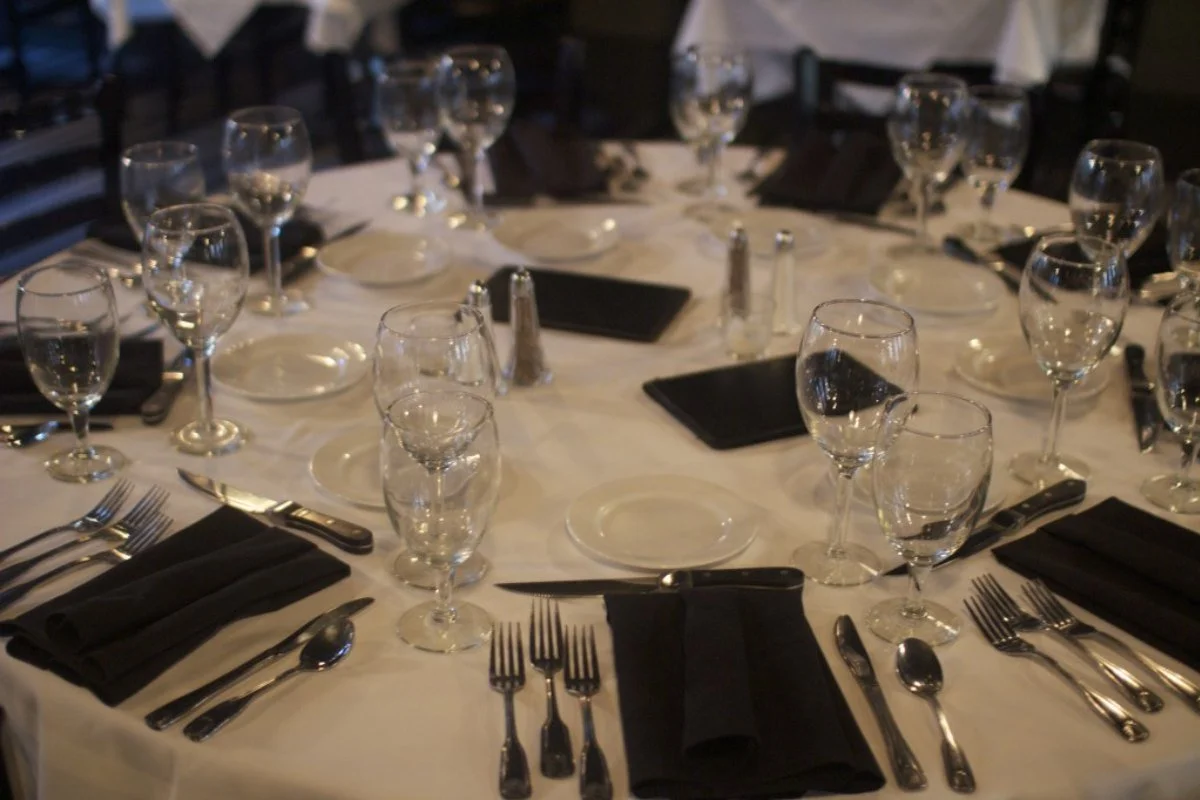 A formal dining table set with multiple wine glasses, water glasses, black napkins, and silverware on a white tablecloth, ready for a meal.