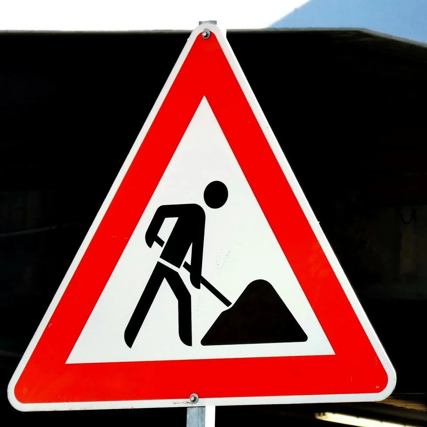 Panneau de signalisation orange avec un symbole de travailleur de la construction déposant du sable ou du gravier.