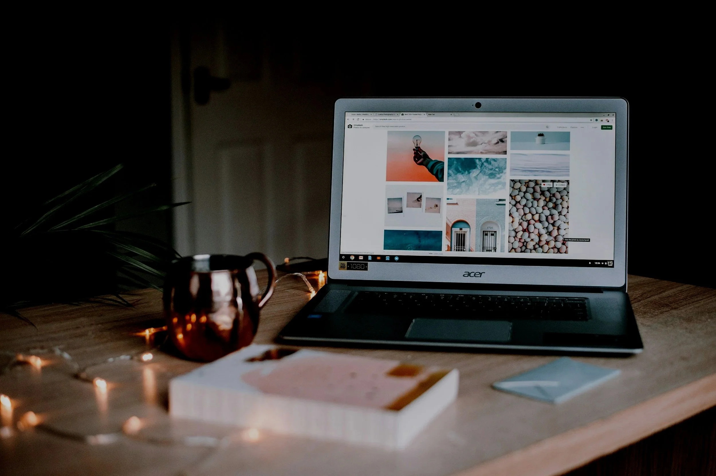 Un ordinateur portable affichant une galerie d'images sur son écran, placé sur une table en bois avec une tasse en cuivre réfléchissante et des papiers.