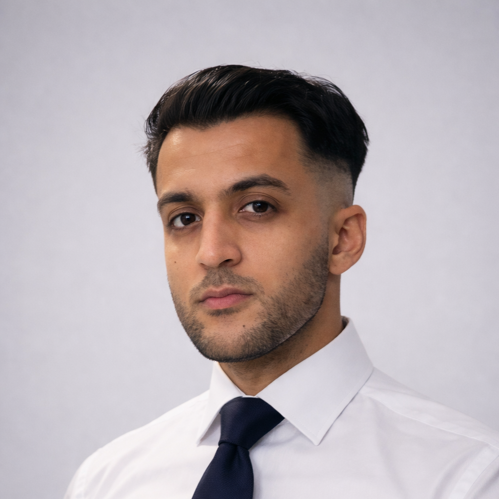 A portrait of a young man with dark hair, styled neatly, wearing a white shirt and a dark tie, against a plain light gray background.