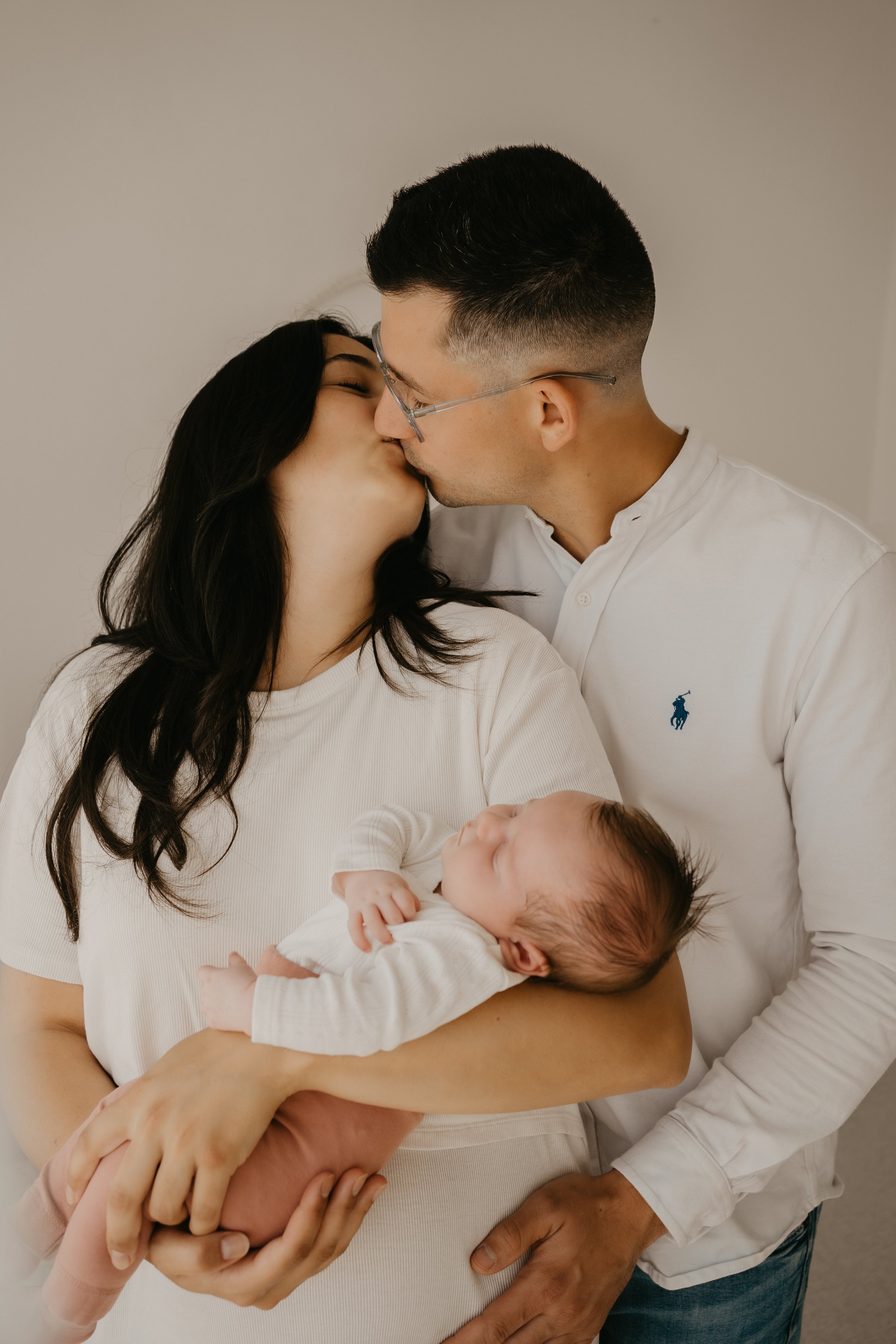 Ein Paar, vermutlich Eltern, küssen sich liebevoll, während die Mutter ein Baby hält.