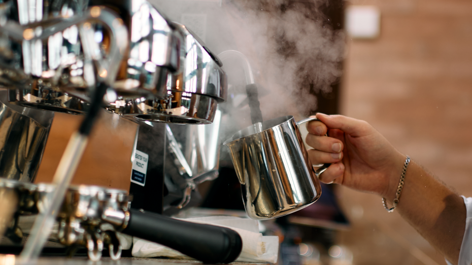 En person som lager kaffe med en espressomaskin, damper steam fra en melkekanne.
