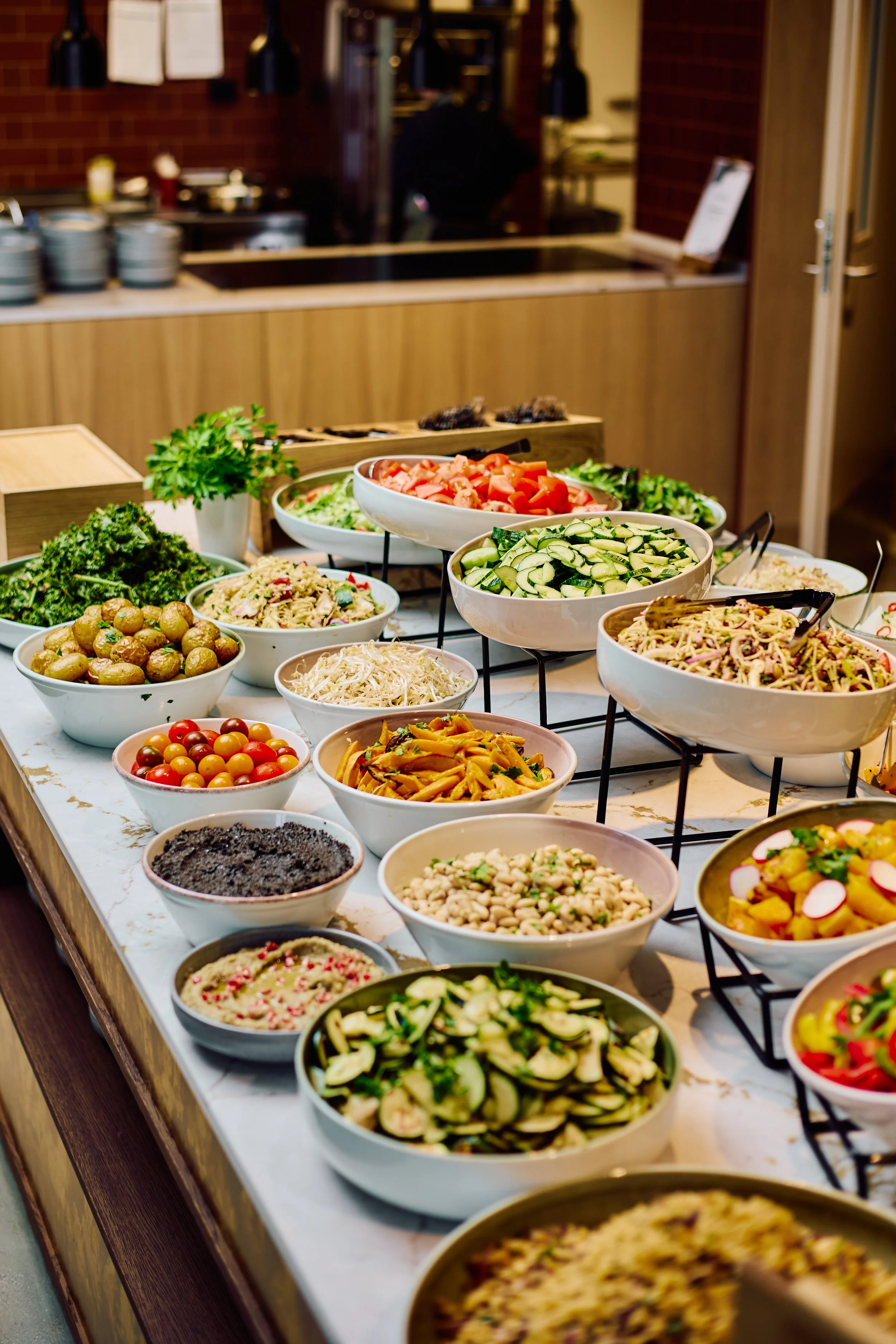Brett med ulike salat- og grønnsaksboller på en buffetbord.