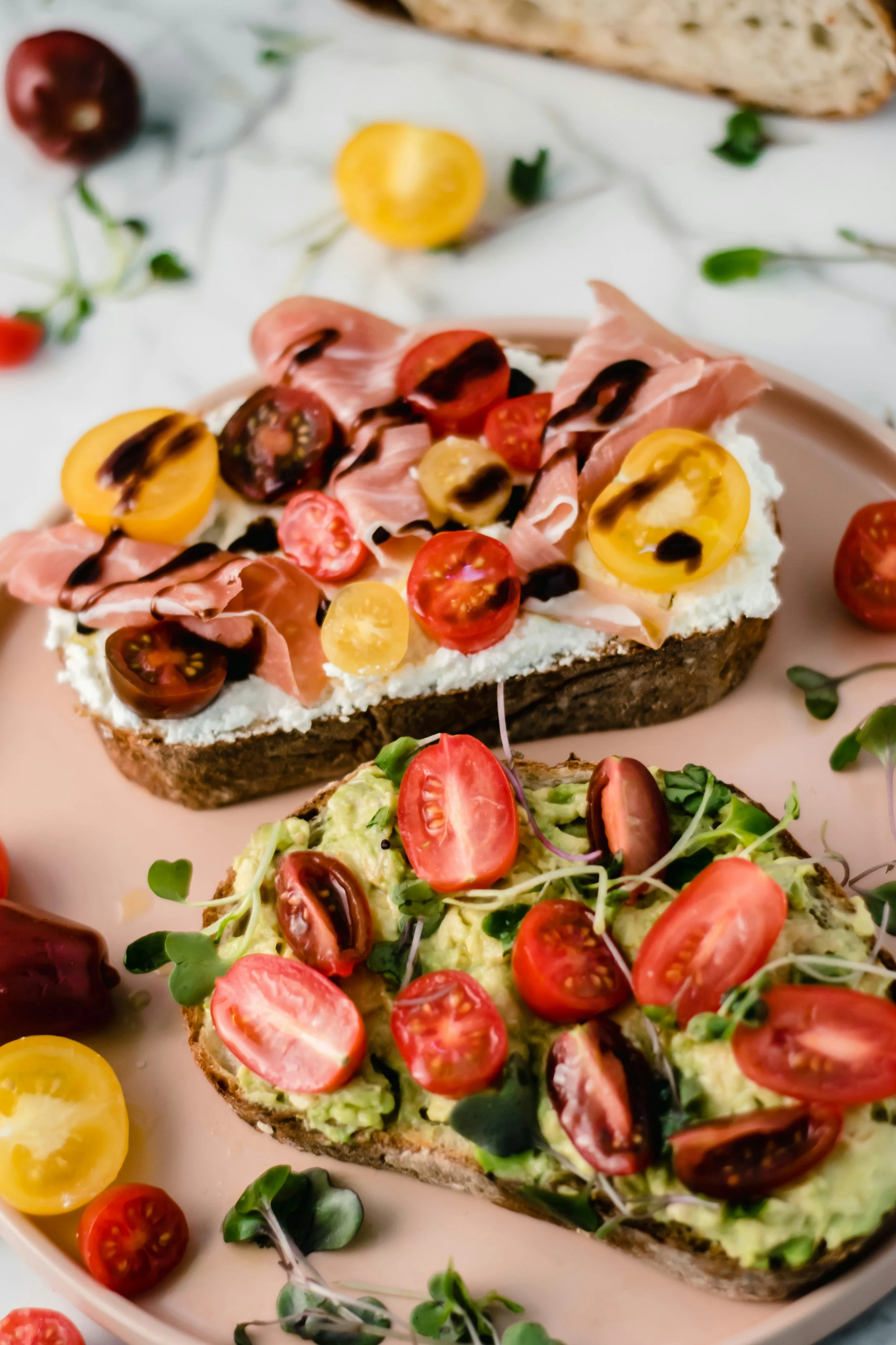 To av brødskivene er smurt med avocado, toppet med cherrytomater, mikrogrønt, og balsamico glace.