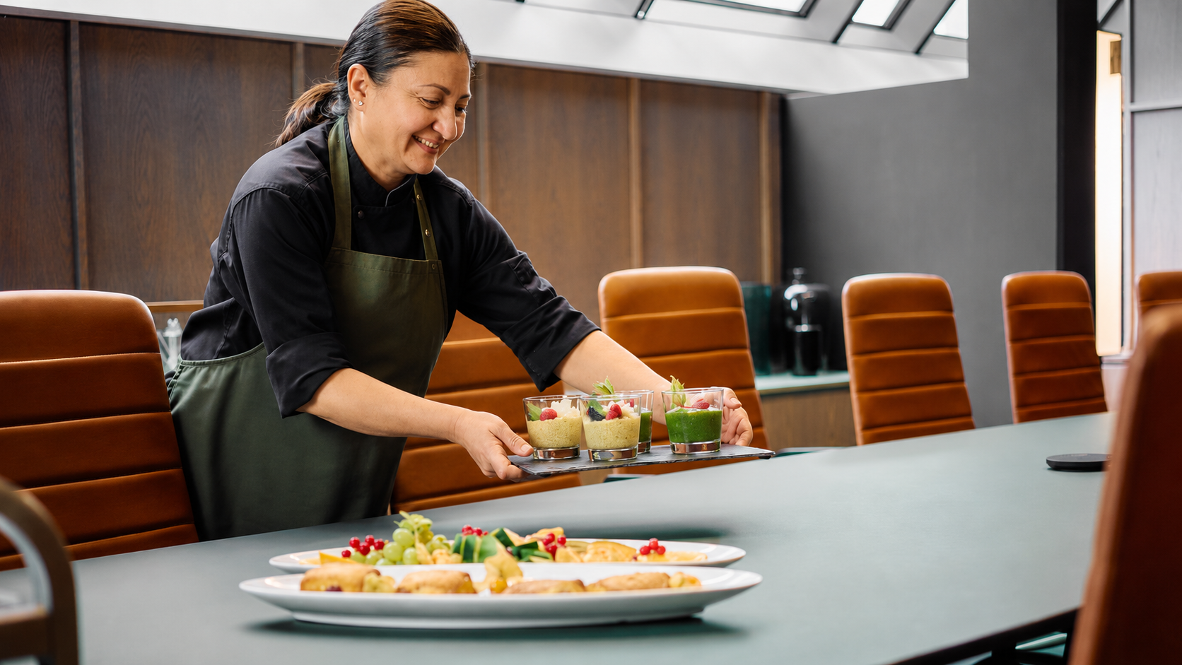 En kvinne i kjøkkenuniform legger fram dessertglass på et konferanserom.