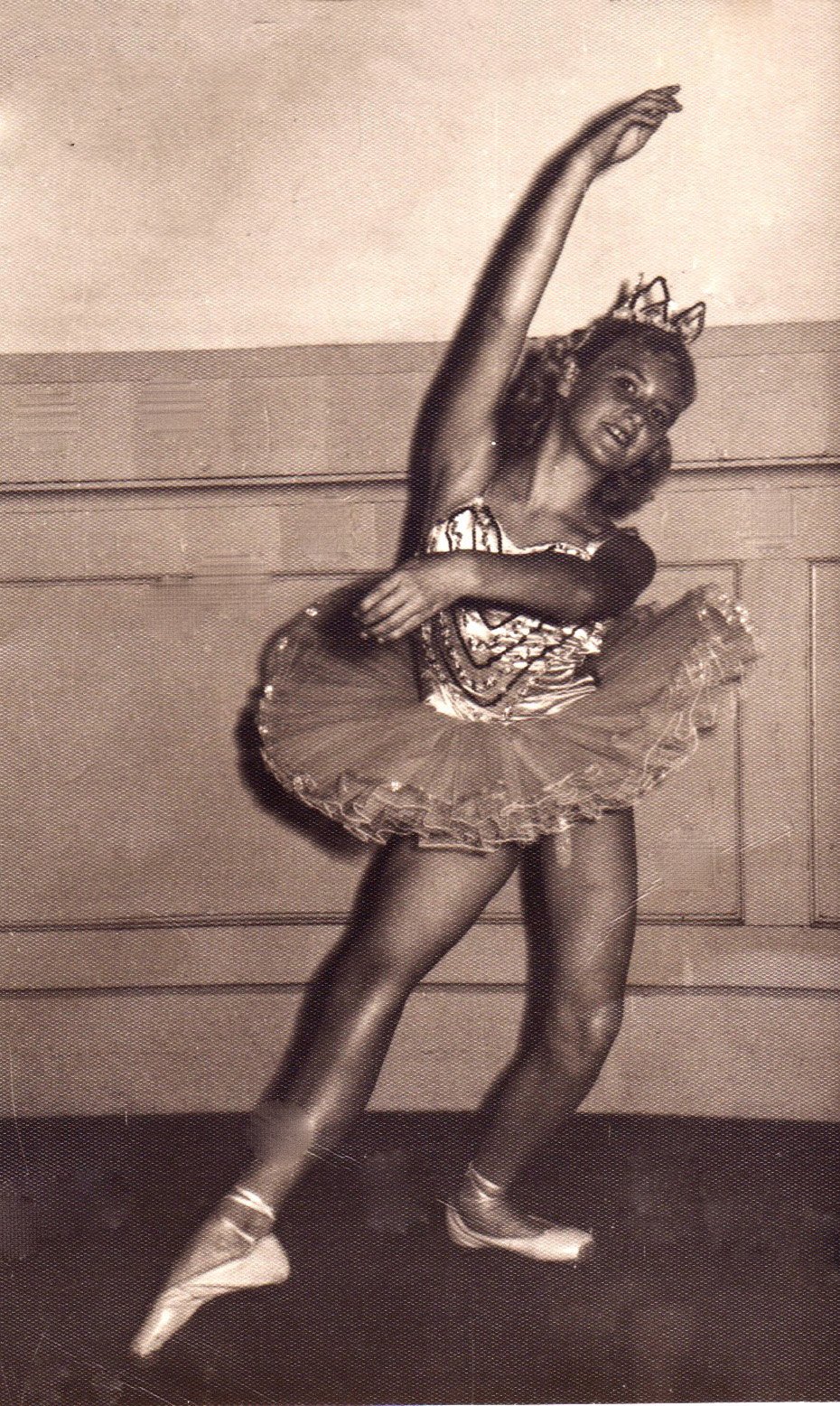 A young girl in a ballet costume with a tutu and ballet shoes performing a dance pose.
